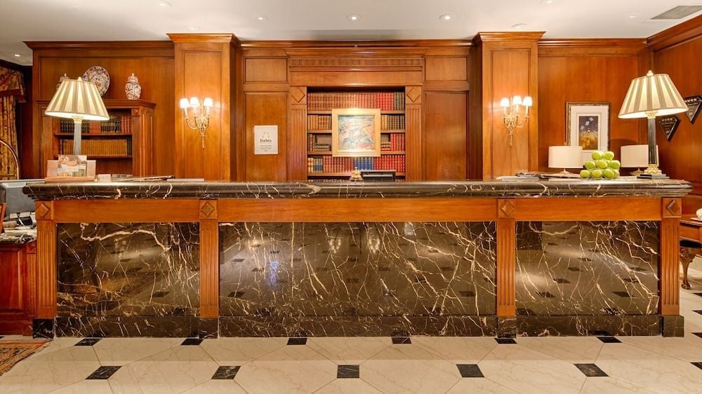 Rich mahogany paneling and veined marble create an intimate library-like atmosphere at the front desk, where crystal sconces cast a warm golden glow.