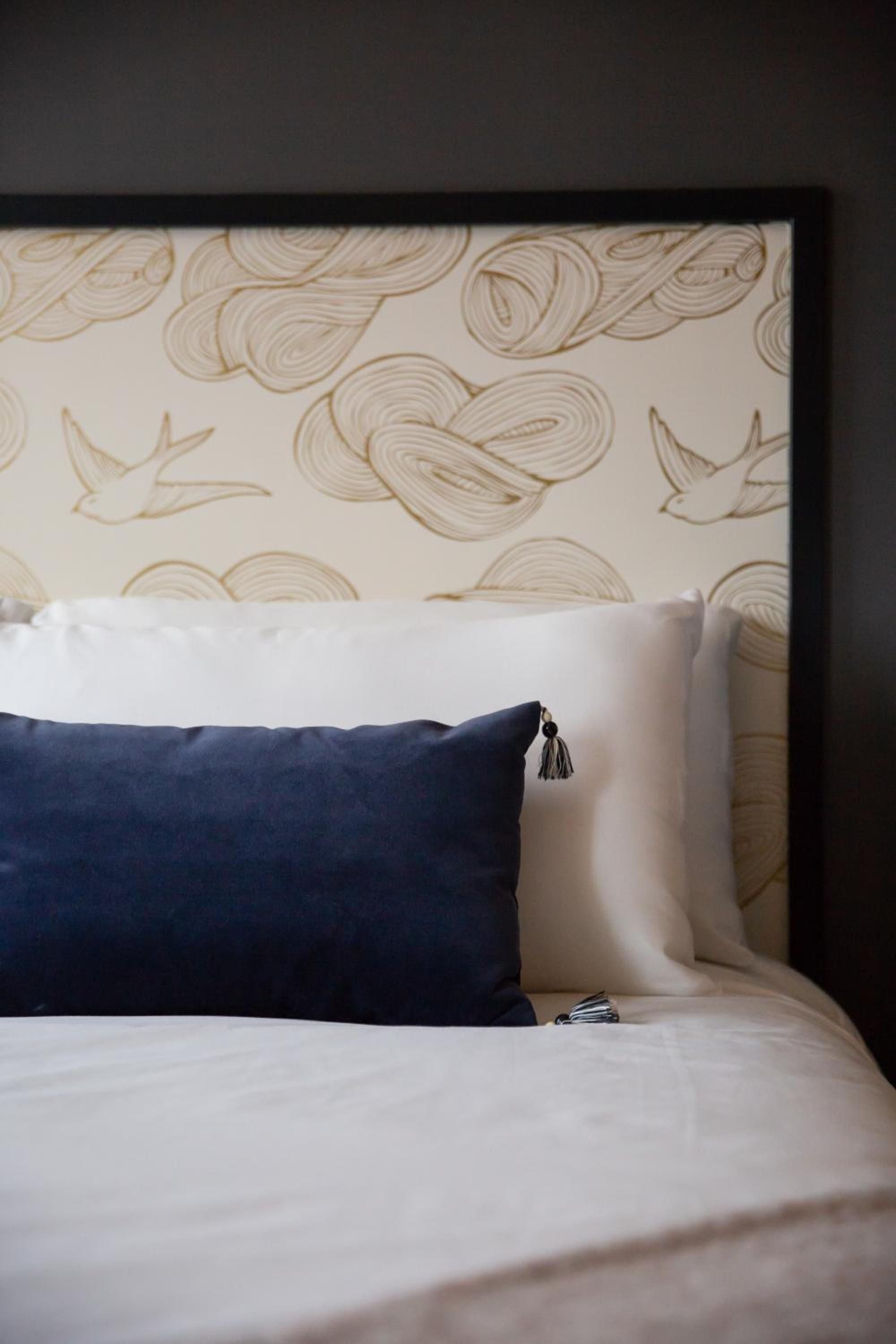 Swallow motifs dance across custom wallpaper above crisp linens, where navy velvet cushions and tassel details create an intimate nautical narrative in guest quarters.