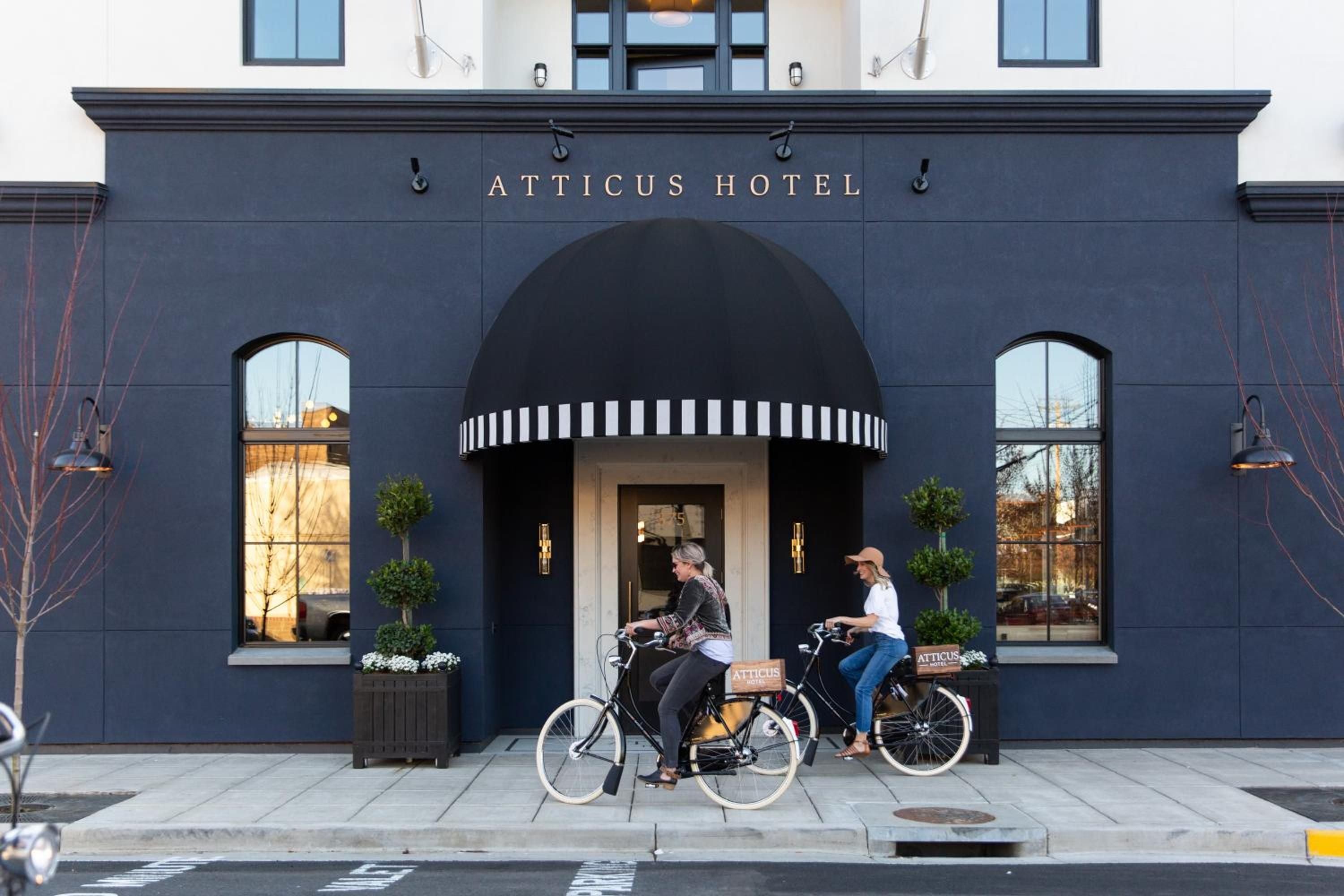 Navy-blue façade and striped awning create striking curb appeal as guests cycle past the boutique hotel's welcoming entrance, framed by topiary planters and brass fixtures.