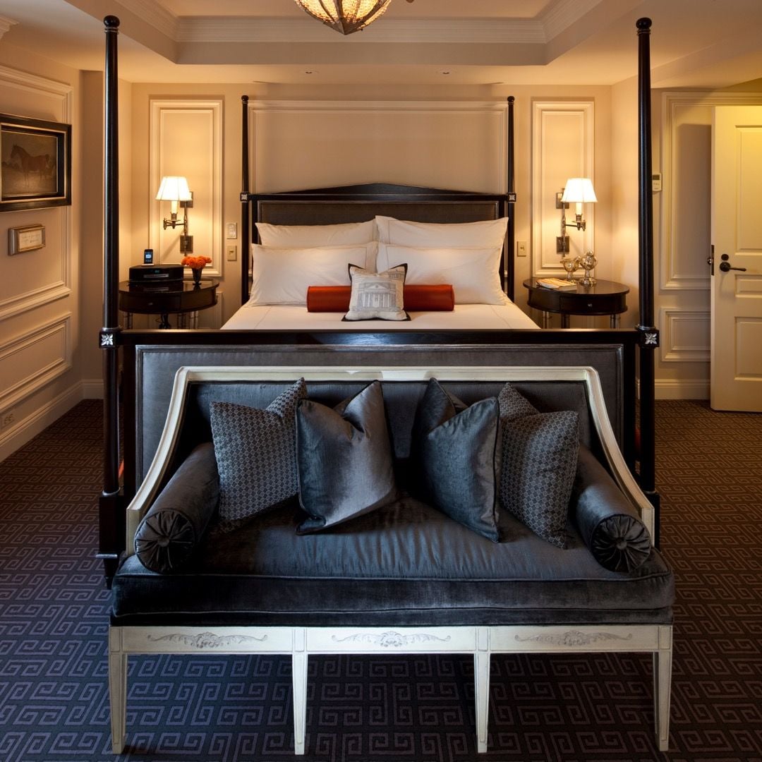 Rich mahogany four-poster beds and navy velvet seating create an atmosphere of refined elegance, where classical moldings meet contemporary luxury in perfect harmony.