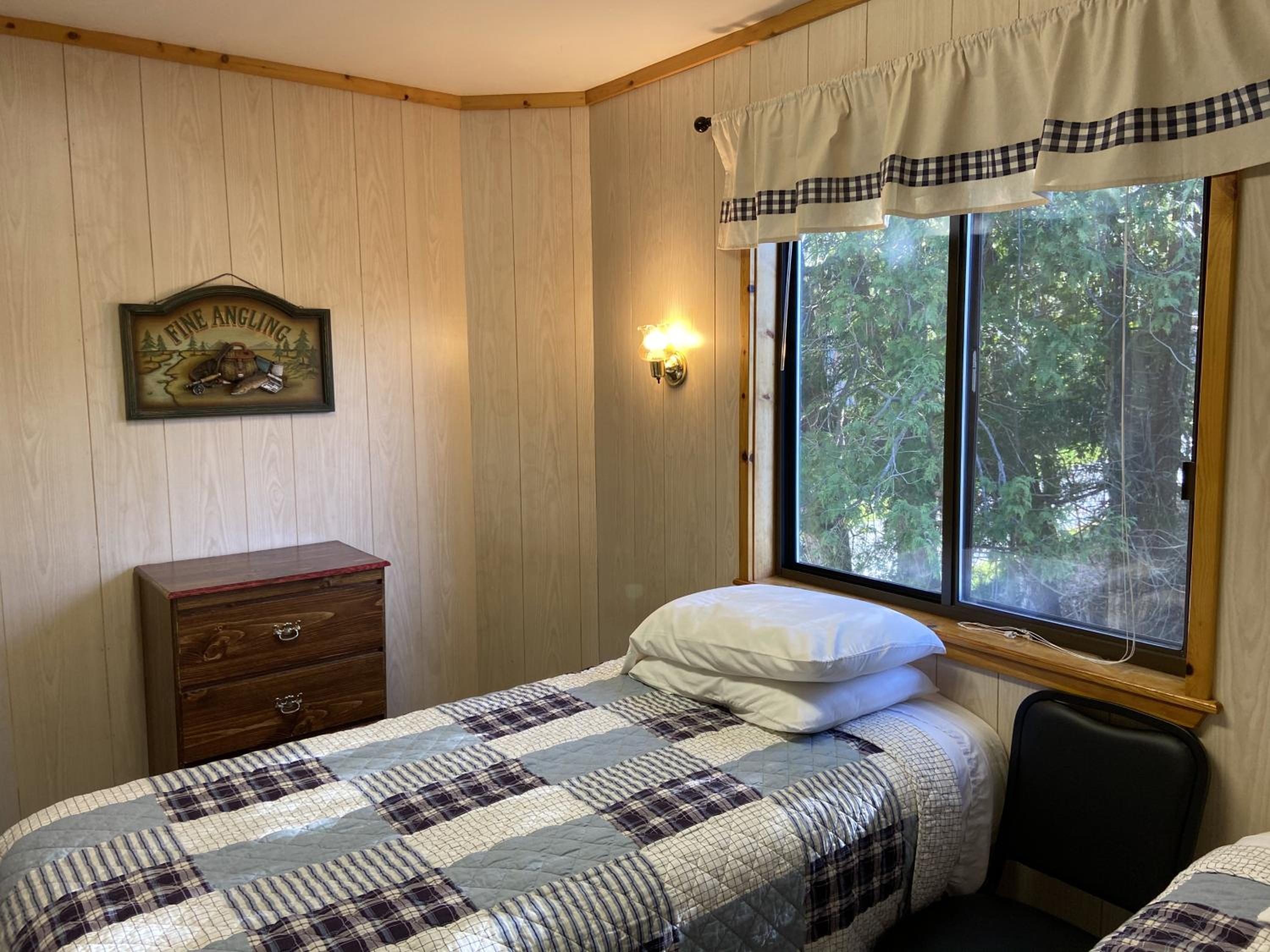 Wood-paneled walls and blue gingham accents create a cozy cabin retreat, where morning light filters through windows overlooking dense Michigan forest.