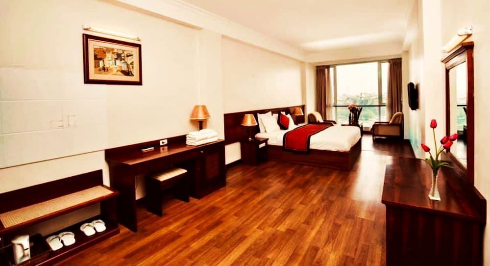 Rich mahogany furnishings and gleaming hardwood floors create an elegant retreat, where warm amber lighting reflects off polished surfaces and city views beckon beyond flowing curtains.
