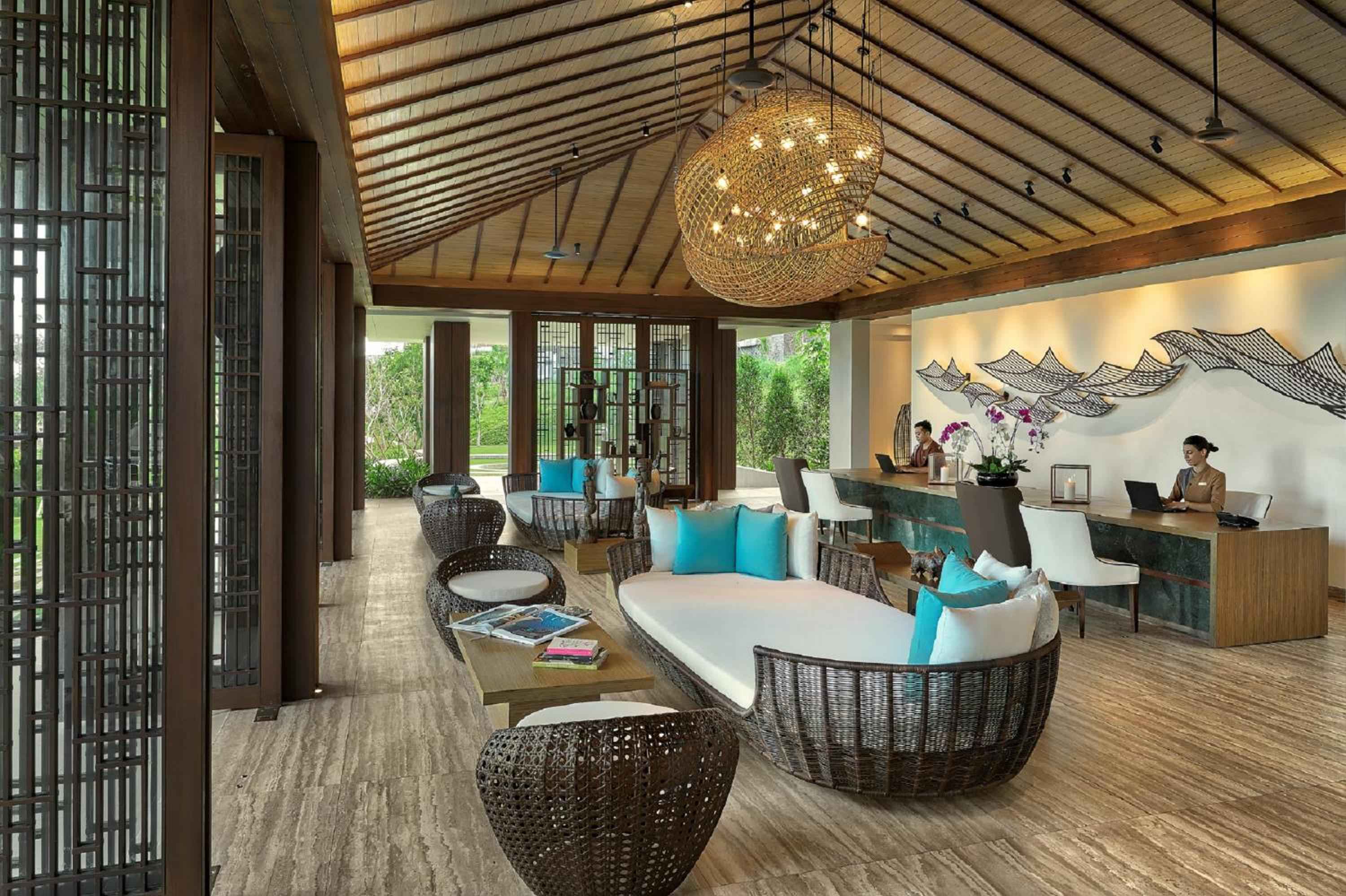 Woven rattan seating and a sculptural pendant light create an inviting lobby where natural textures meet contemporary design beneath soaring wooden beams.