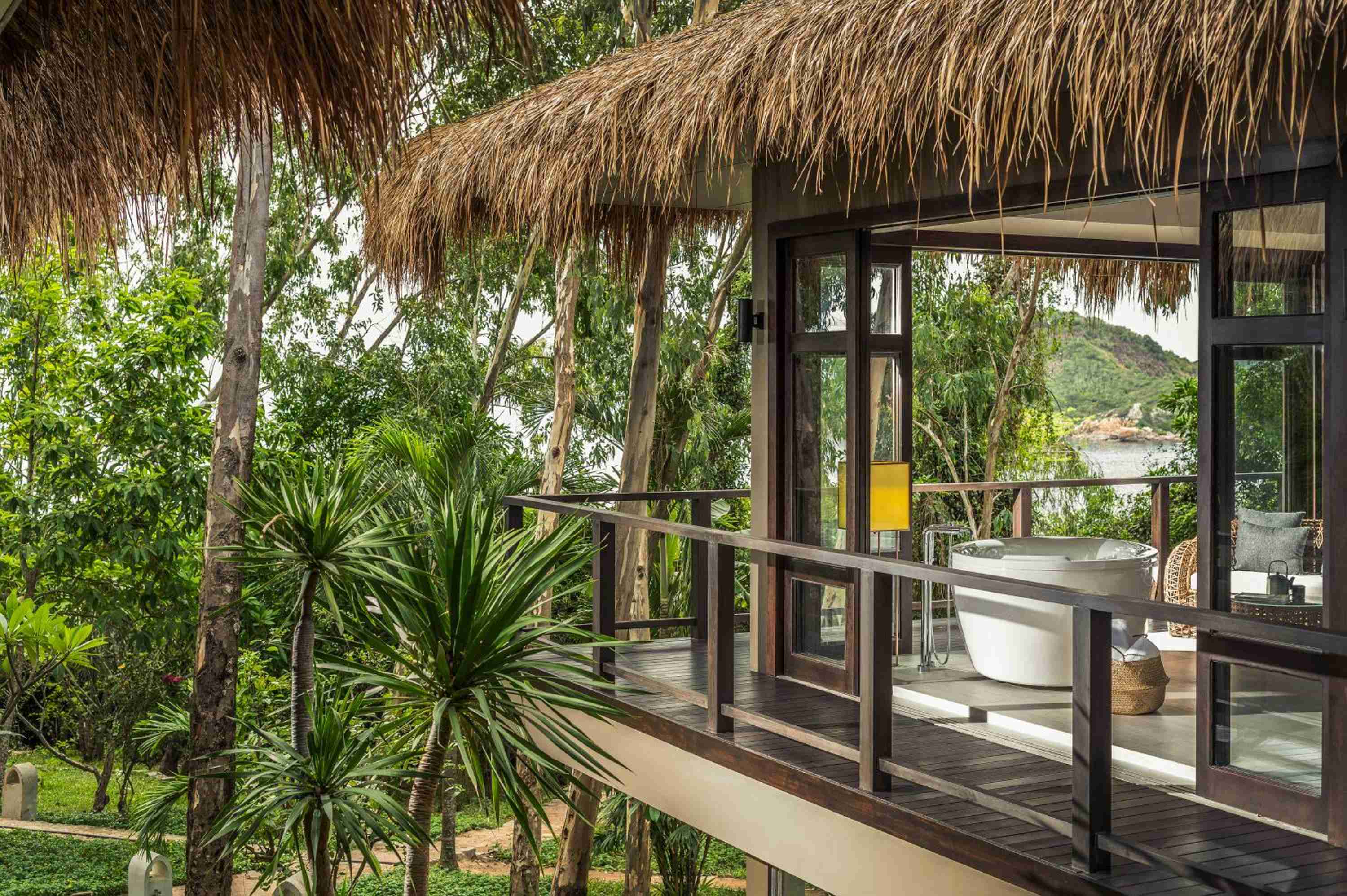 Open-air bathroom pavilion with freestanding tub overlooks emerald jungle canopy, where salt breezes mingle with tropical birdsong through thatched palm fronds.