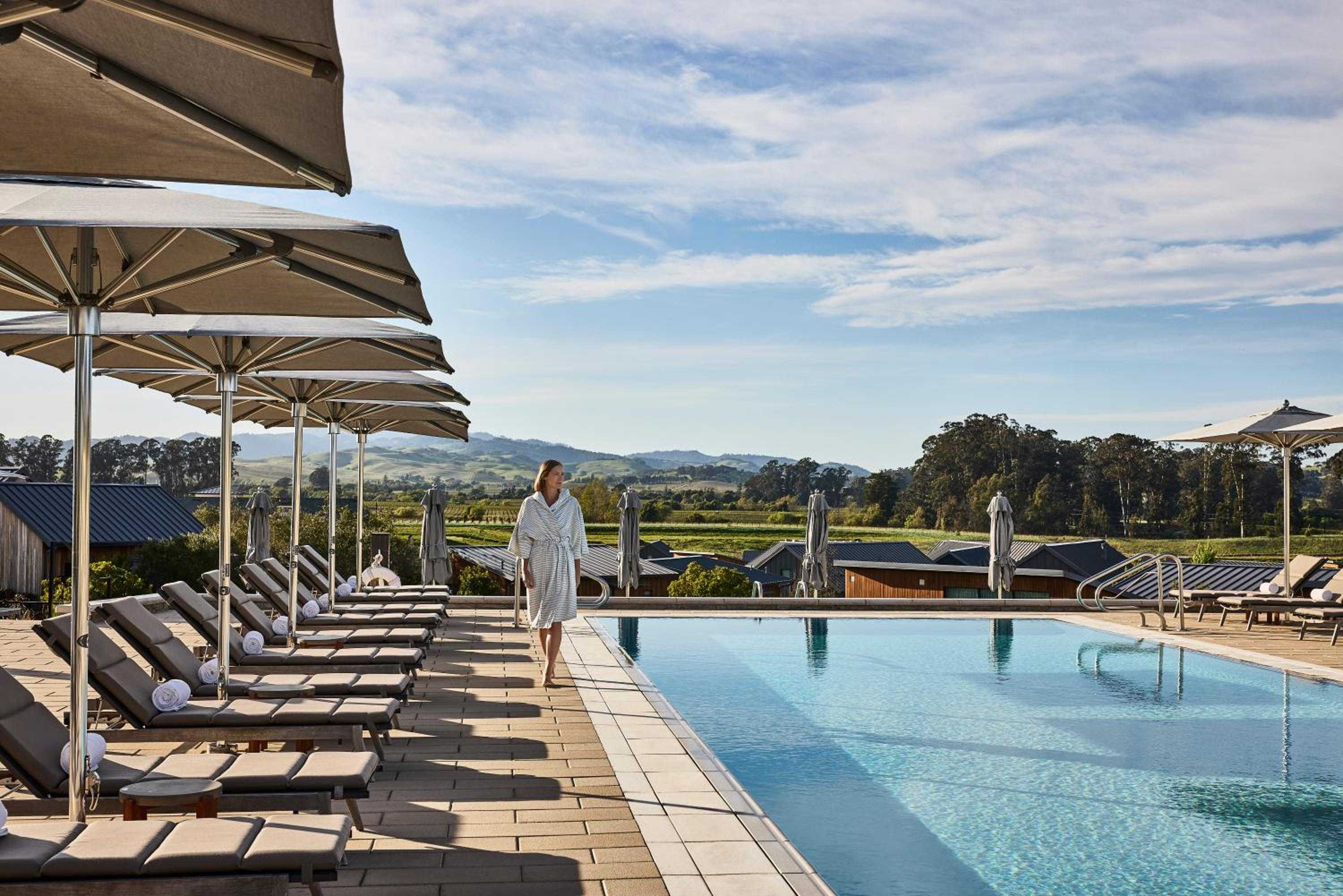 Sun-warmed stone surrounds the infinity pool where Napa Valley's rolling vineyards stretch endlessly beyond, umbrellas casting geometric shadows across pristine loungers.