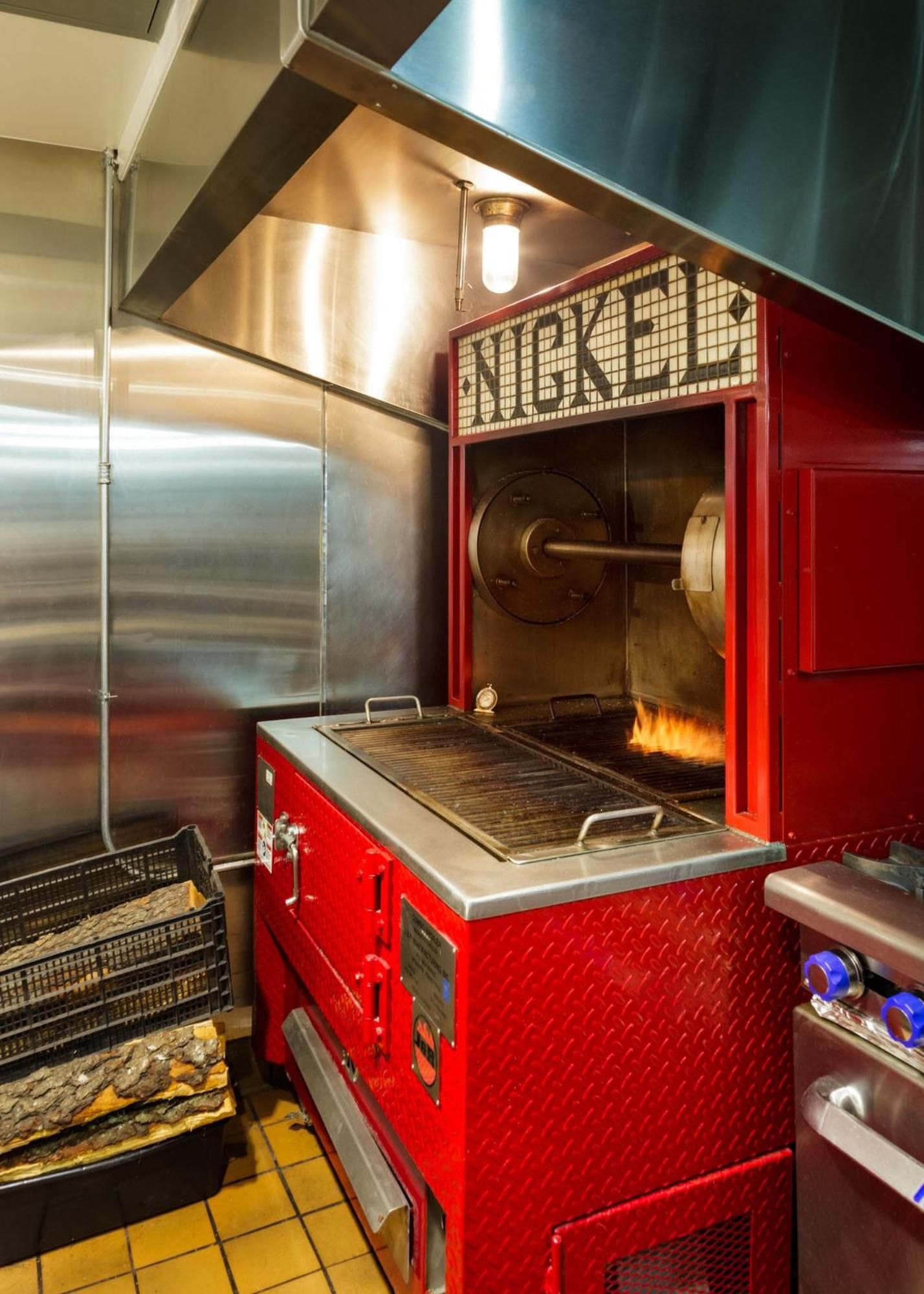 Vintage-inspired red nickel machine anchors the open kitchen, where flames dance behind glass and gleaming stainless steel creates an industrial-chic dining theater.