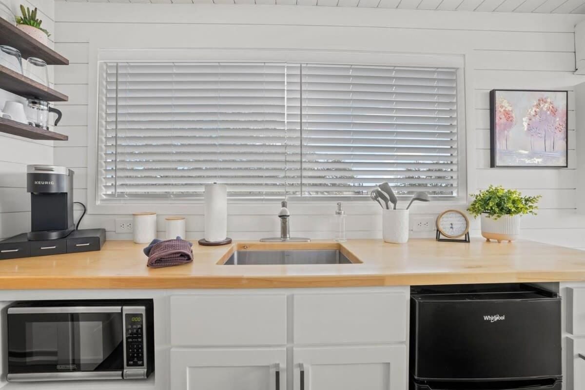 Butcher block counters and white shiplap walls create a serene workspace where morning coffee rituals unfold against soft natural light filtering through plantation blinds.