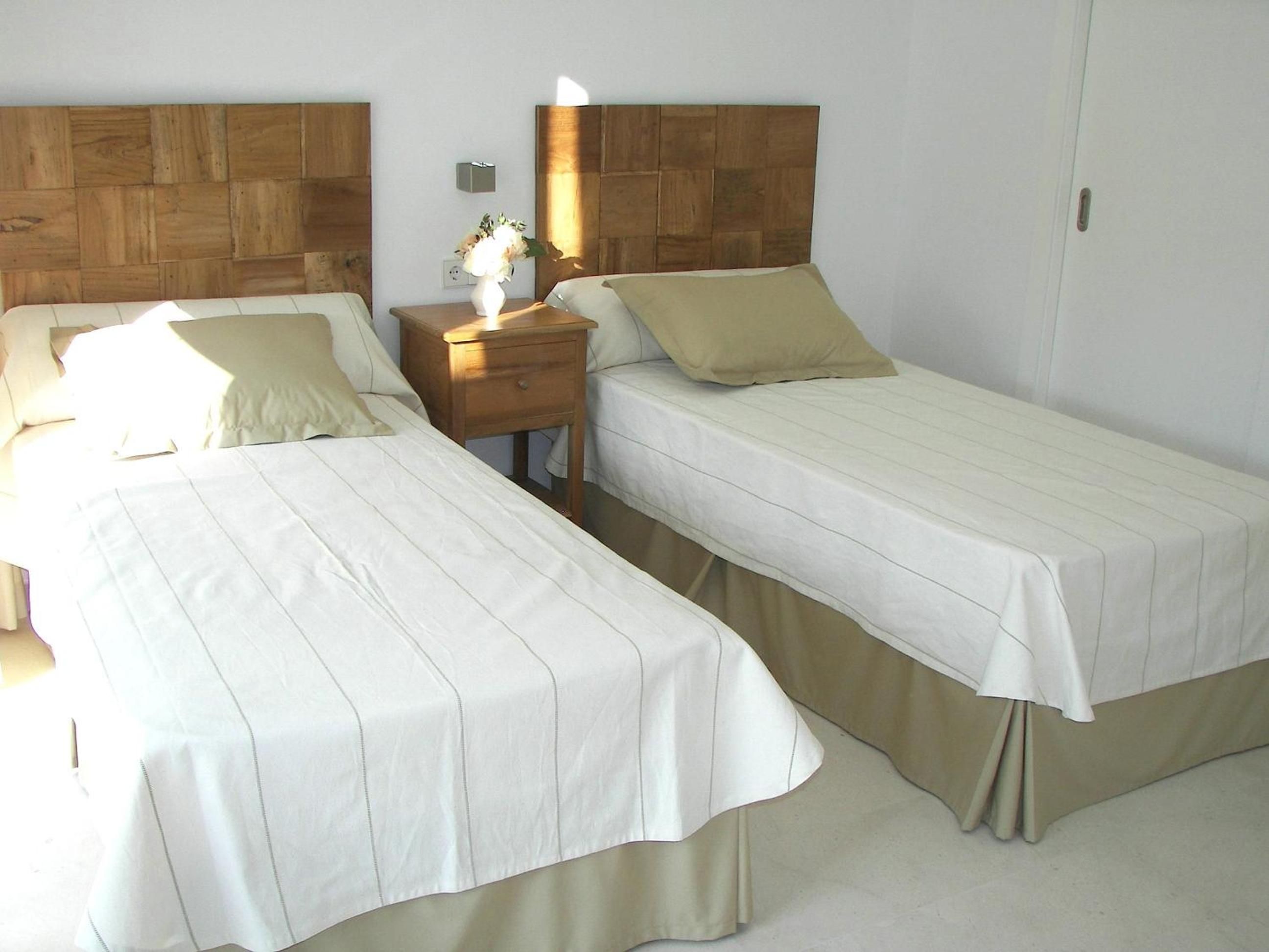 Twin beds with geometric wood headboards create a serene sanctuary, where morning light streams across crisp white linens and polished floors invite barefoot wandering.