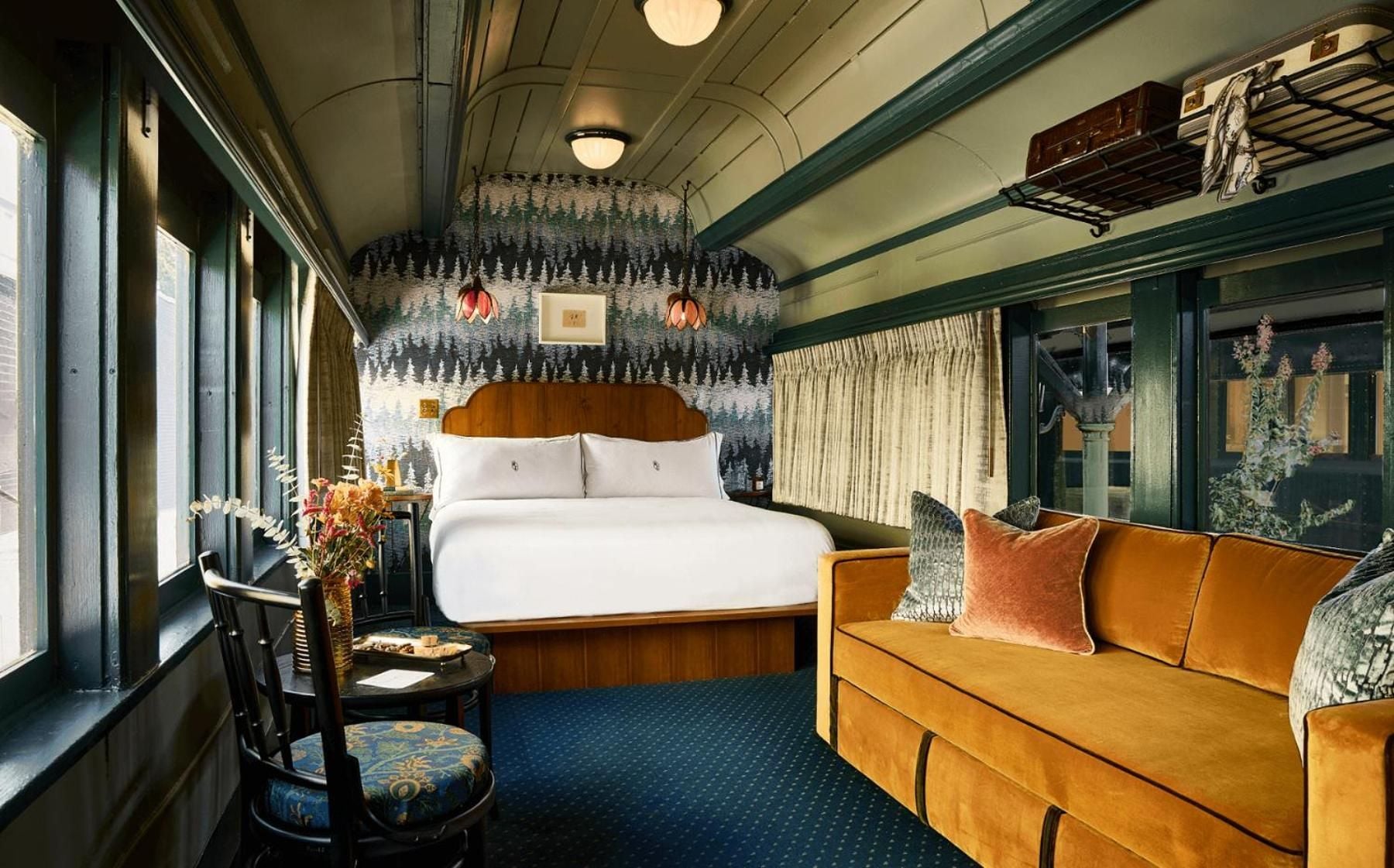 Forest-green millwork and botanical wallpaper create an enchanting railway carriage suite, where curved ceilings and vintage brass details transport guests to a bygone era of luxury train travel.