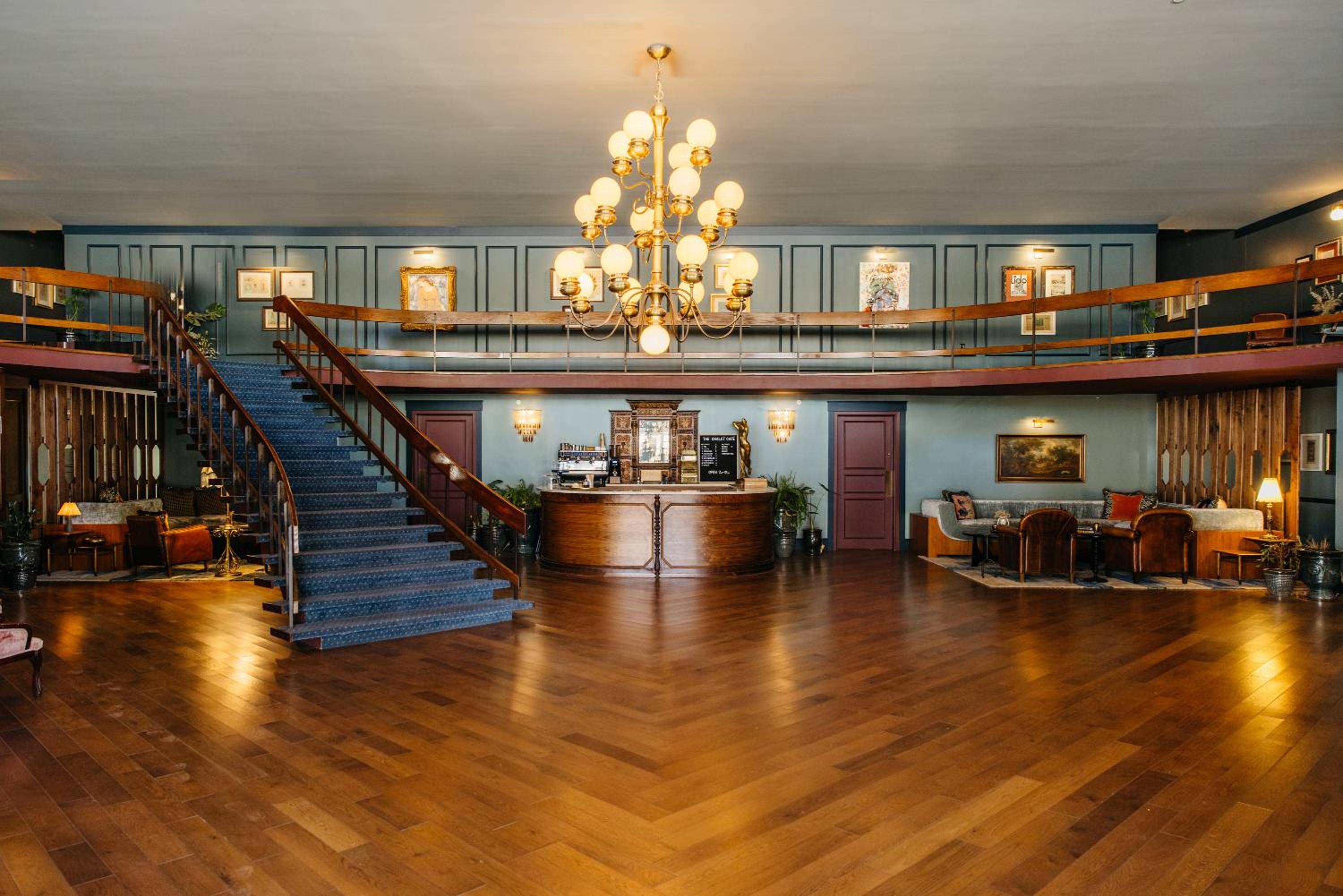 Grand brass chandelier illuminates polished hardwood floors while a sweeping staircase curves toward the mezzanine, creating an atmosphere of refined Southern hospitality.