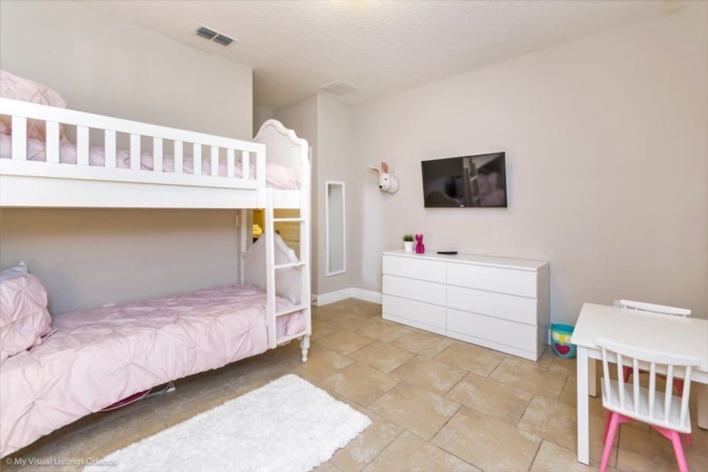 Pink bedding softens the white bunk beds in this cheerful children's room, where natural light streams across warm tile floors and modern furnishings create a playful retreat.