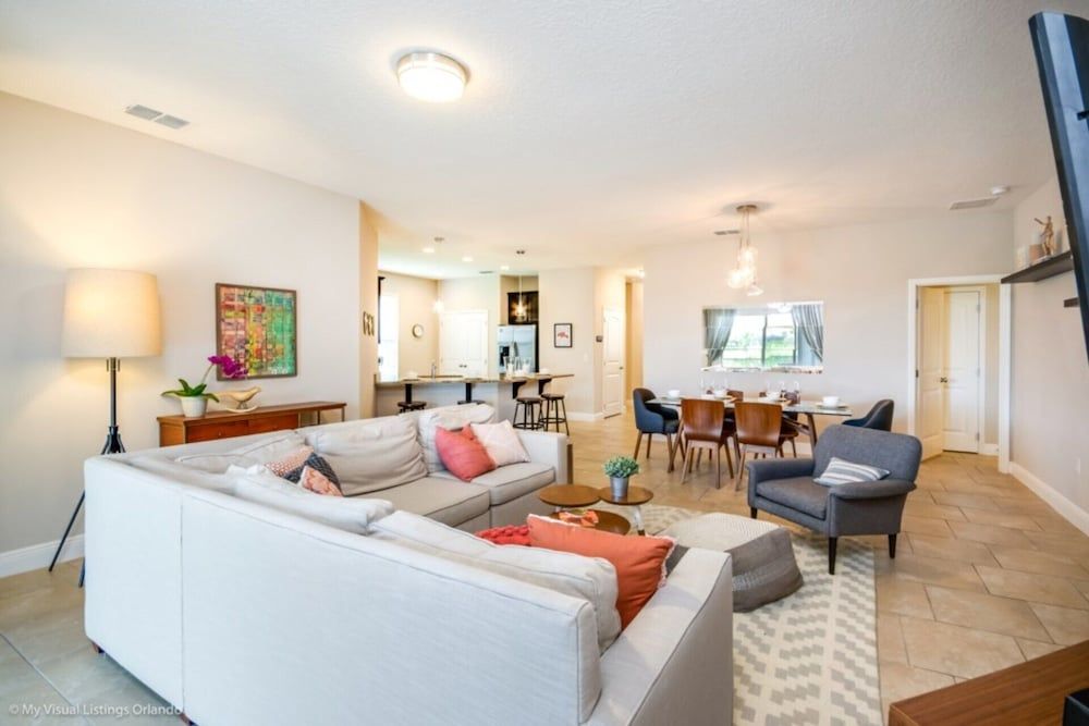 Open-concept living flows seamlessly from coral-accented sectional to warm wood dining table, where coastal light filters through crisp white spaces designed for effortless family gathering.
