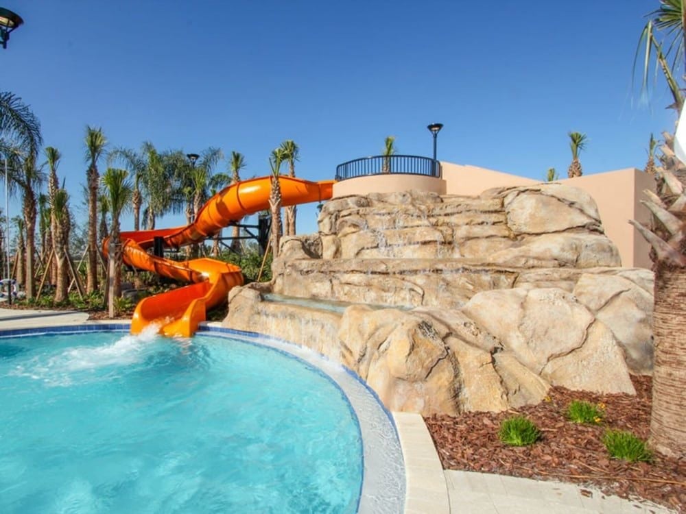 Spiraling orange waterslide winds around artificial rock formations, creating a desert oasis playground where palm trees frame crystal-clear waters under endless Florida skies.