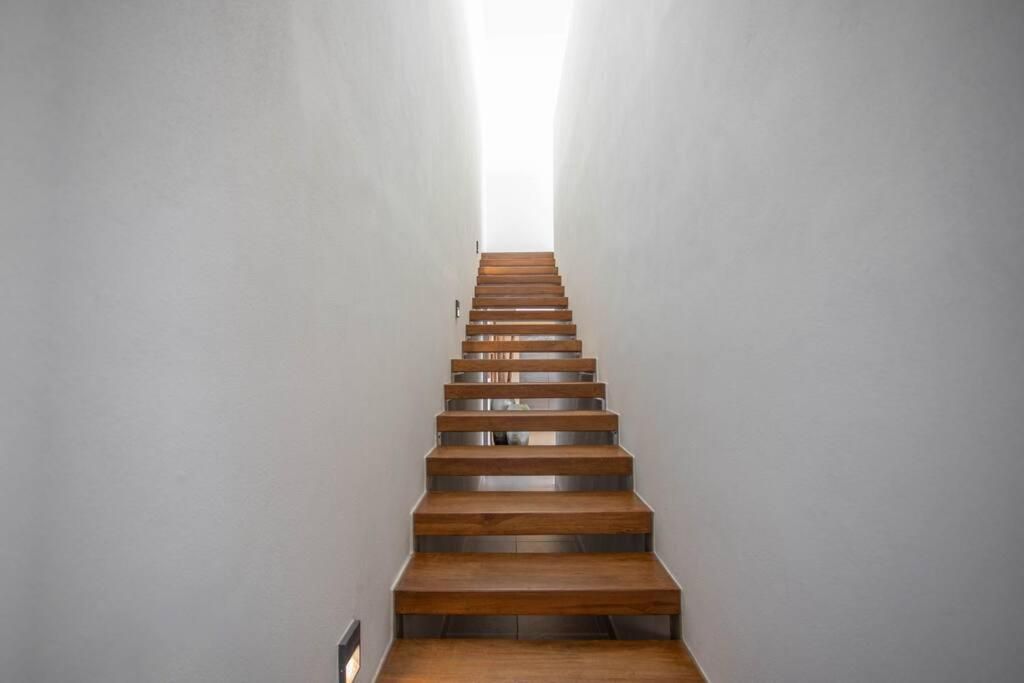Floating walnut treads ascend between pristine white walls, their open risers creating dramatic shadows while natural light beckons from the upper level.