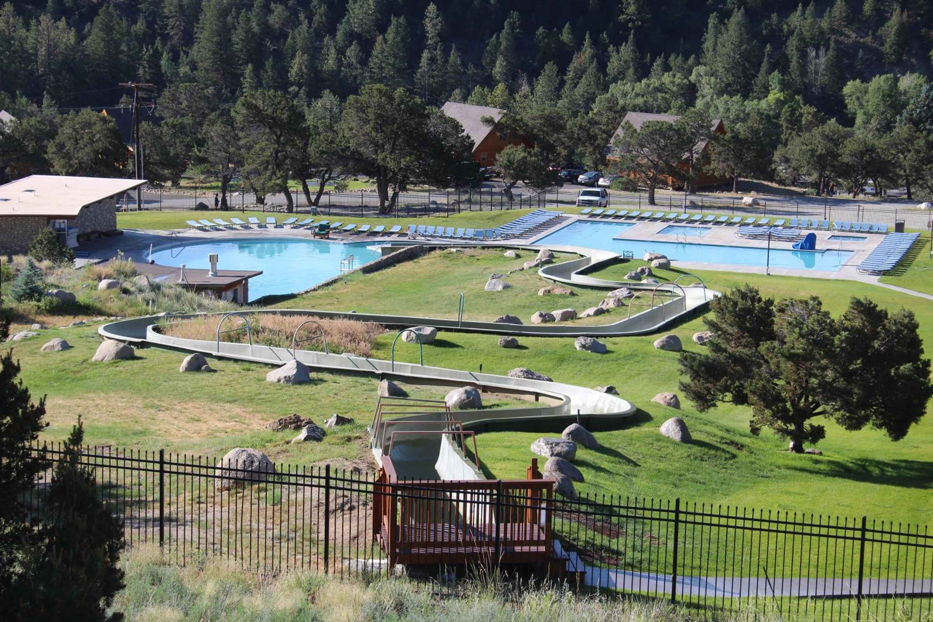 Winding alpine slides snake through manicured grounds past the resort's expansive swimming pools, where Rocky Mountain wilderness creates a dramatic forested backdrop for family recreation.