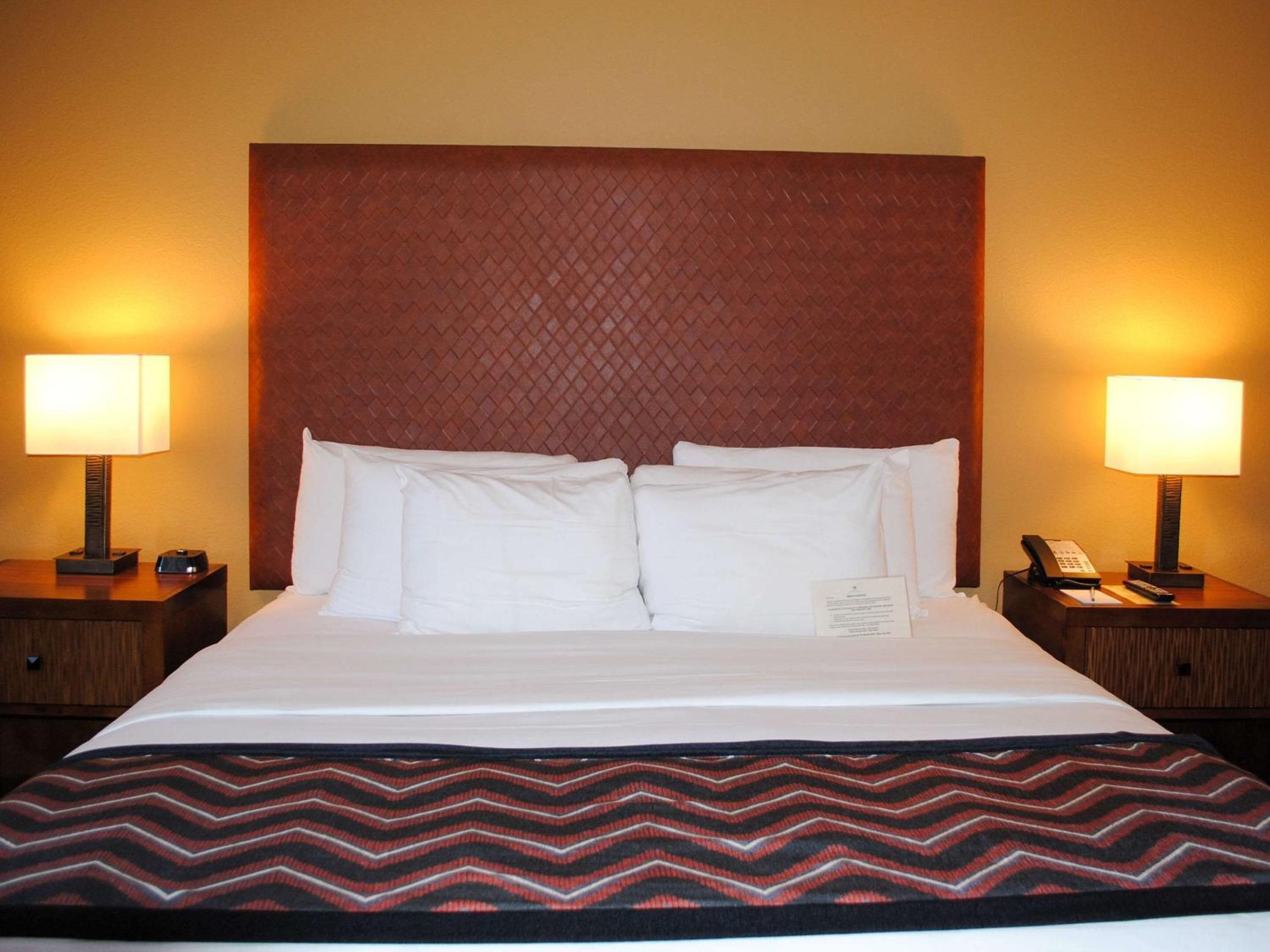 Warm amber lighting and a distinctive woven leather headboard create an inviting retreat, while chevron-patterned throws add southwestern flair to crisp white linens.