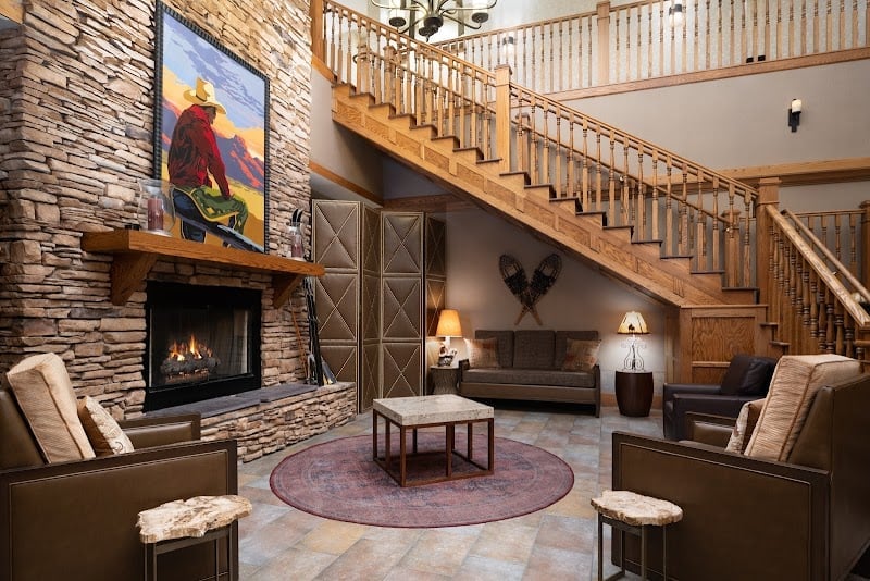 Rustic stone fireplace and soaring timber staircase create mountain lodge ambiance, while leather seating and Native American art add authentic Western warmth to the welcoming lobby.