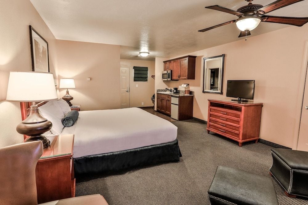 Warm wood furnishings and a compact kitchenette create an inviting extended-stay atmosphere, while soft lighting casts a golden glow across plush carpeting.