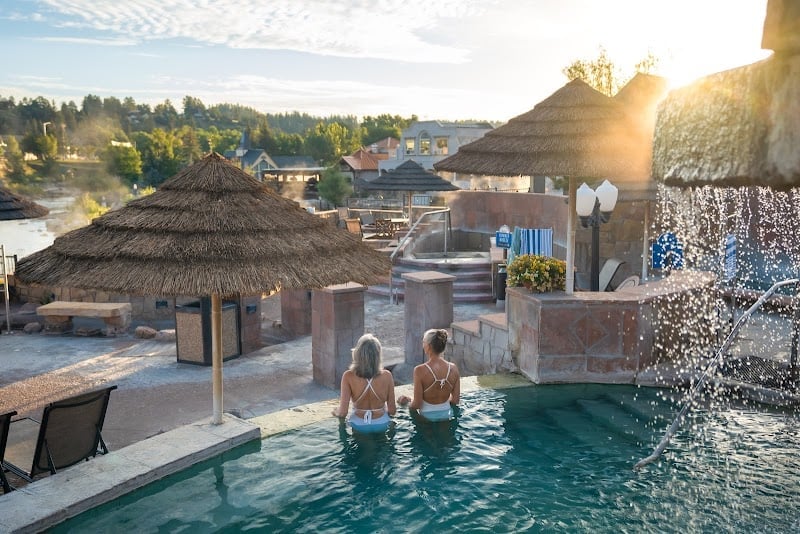 Golden hour light bathes the thermal pools as guests soak beneath thatched umbrellas, mountain views stretching beyond this serene wellness sanctuary.