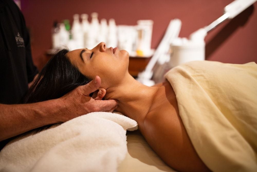 Skilled hands work tension away during a signature treatment, where warm lighting and carefully curated products create an atmosphere of pure tranquility.