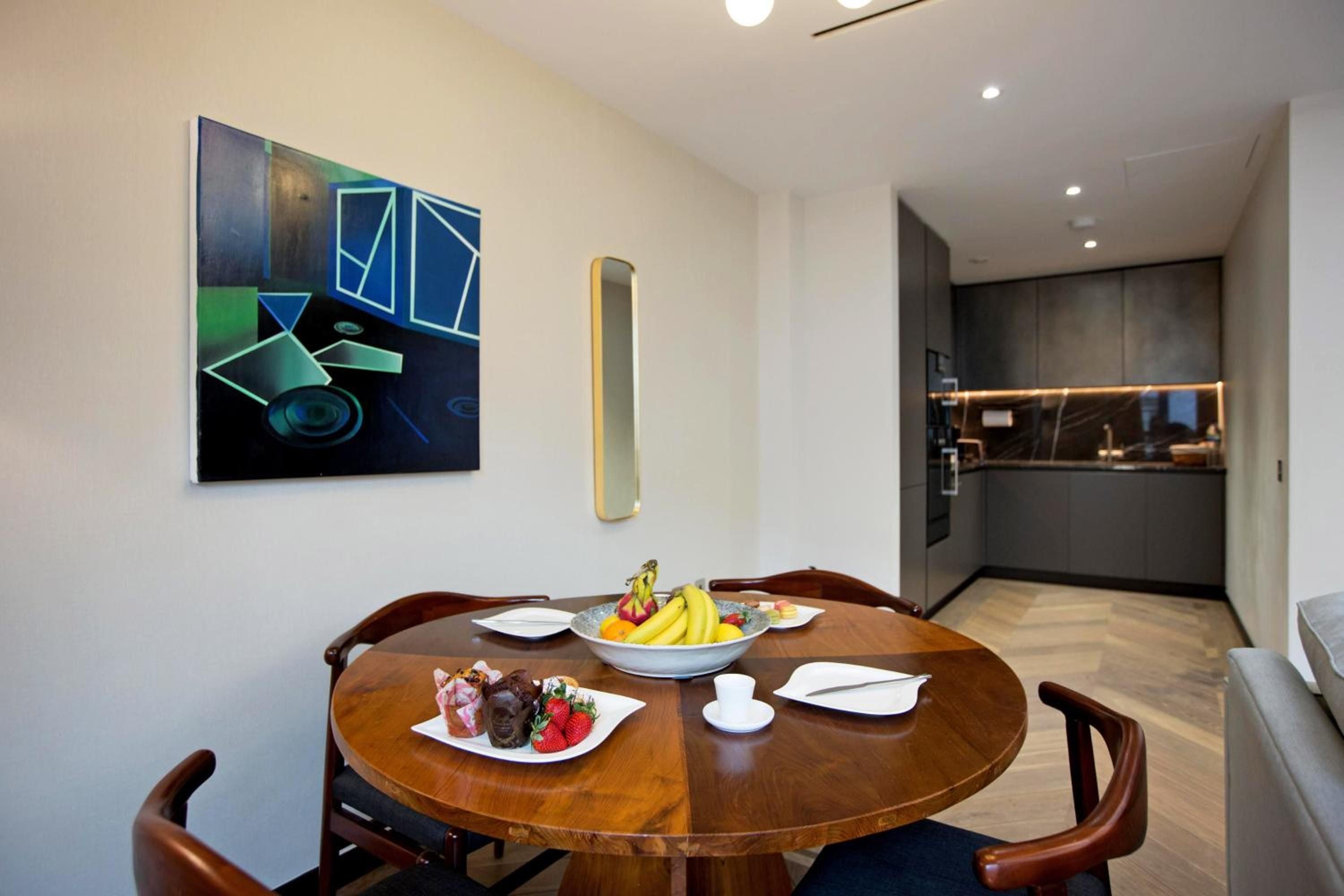 Warm wood grains meet contemporary art in this intimate dining nook, where geometric blues dance above a perfectly set table laden with fresh fruit and delicate pastries.