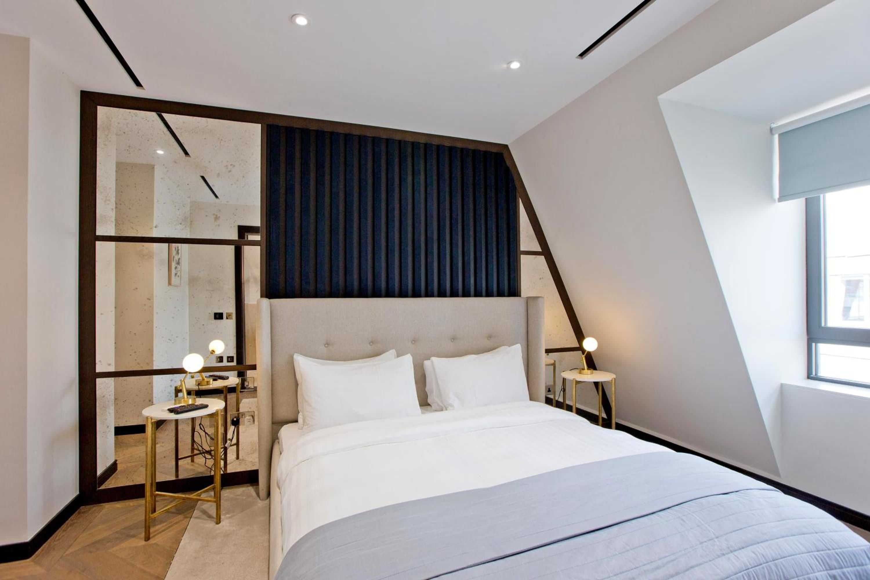 Crisp white linens contrast beautifully with navy velvet headboard paneling, while golden accents and geometric mirrors create sophisticated intimacy in this thoughtfully designed attic suite.