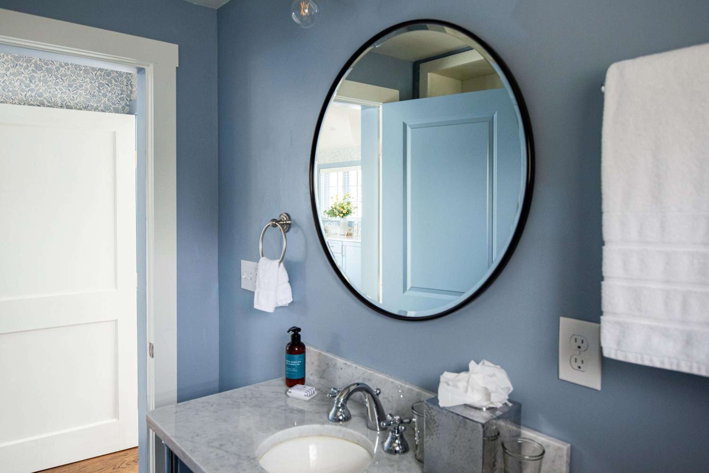 Calming blue walls frame a marble-topped vanity where thoughtful amenities await, while the round black mirror reflects the inn's refined coastal elegance.