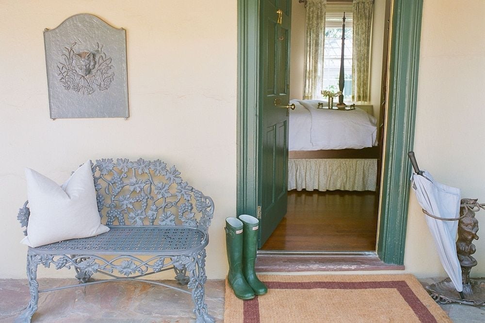 Weathered green doors frame a glimpse into guest quarters, where ornate iron benches and riding boots hint at the inn's equestrian heritage and countryside charm.