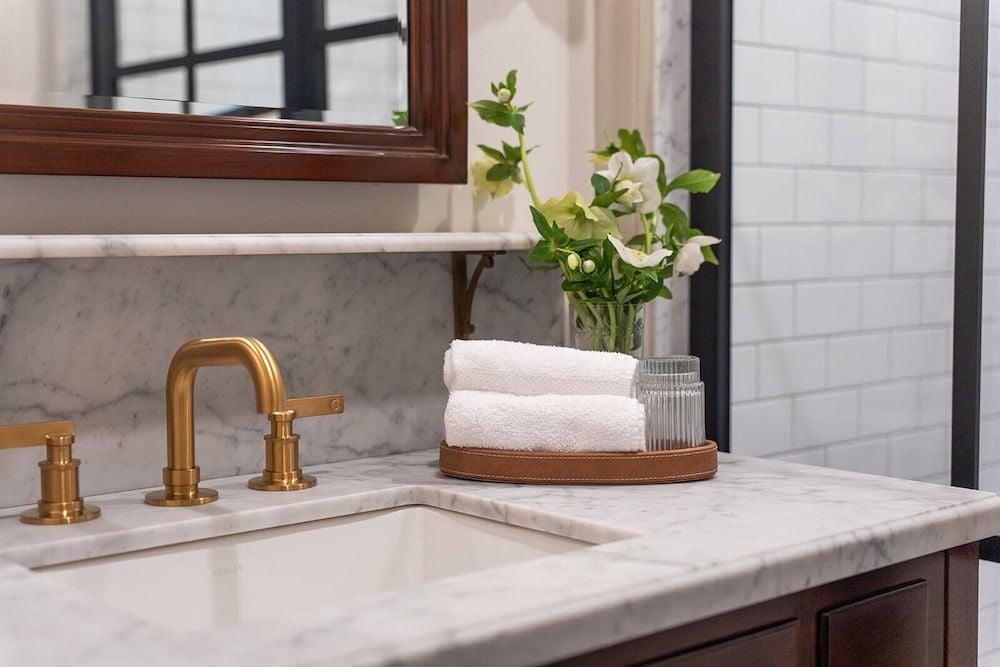 Brass fixtures gleam against Carrara marble while fresh blooms and plush towels create an intimate spa-like retreat in this thoughtfully appointed vanity corner.