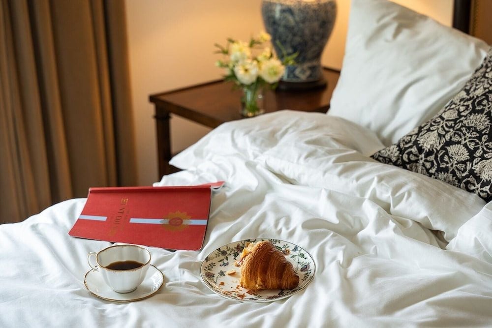 Morning light illuminates crisp white linens where coffee and croissants await, transforming an elegant guest room into a personal sanctuary of indulgence.