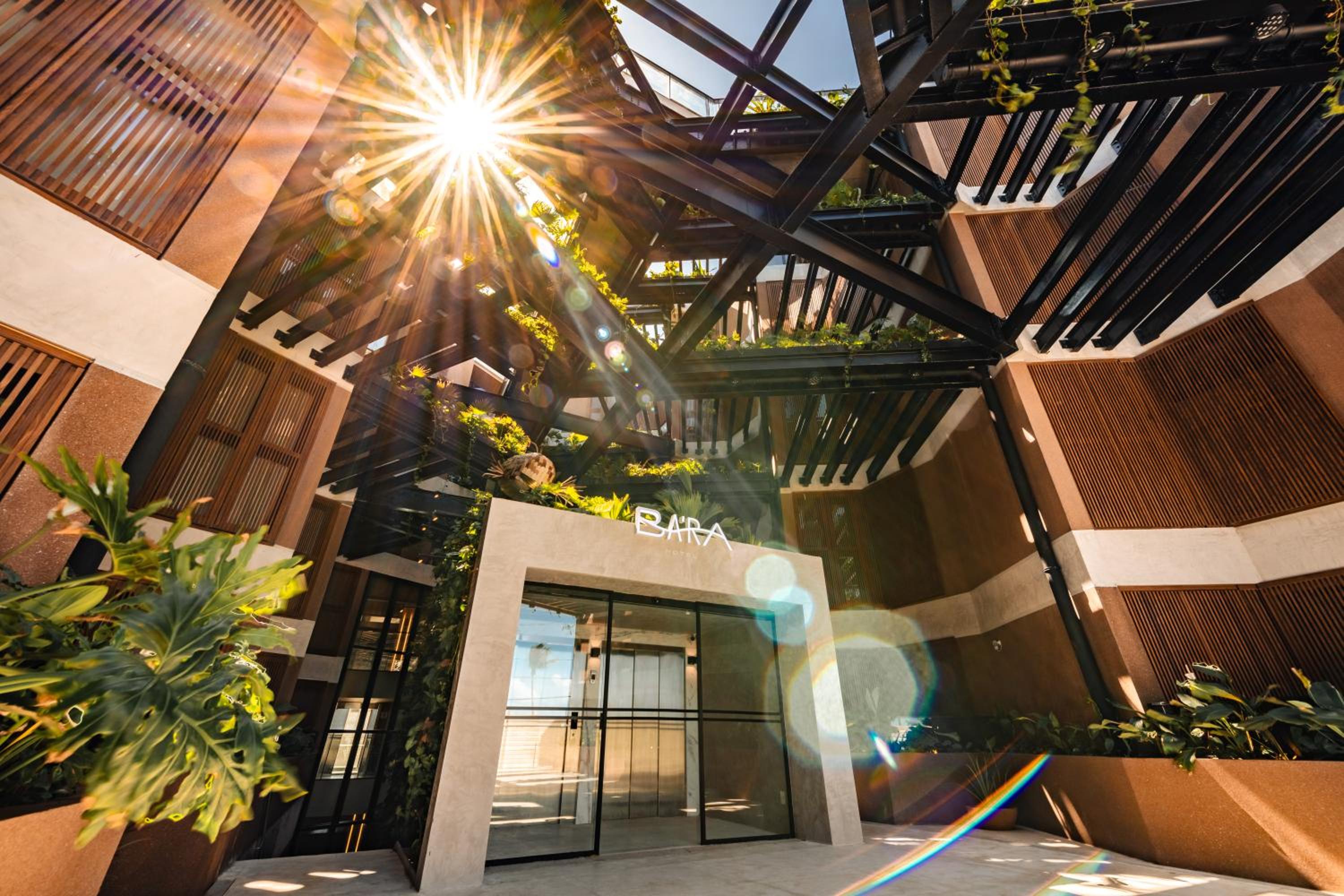Sunlight pierces through the dramatic steel canopy above BA'RA's entrance, creating a dazzling interplay of shadows and warmth that welcomes guests into this architectural sanctuary.