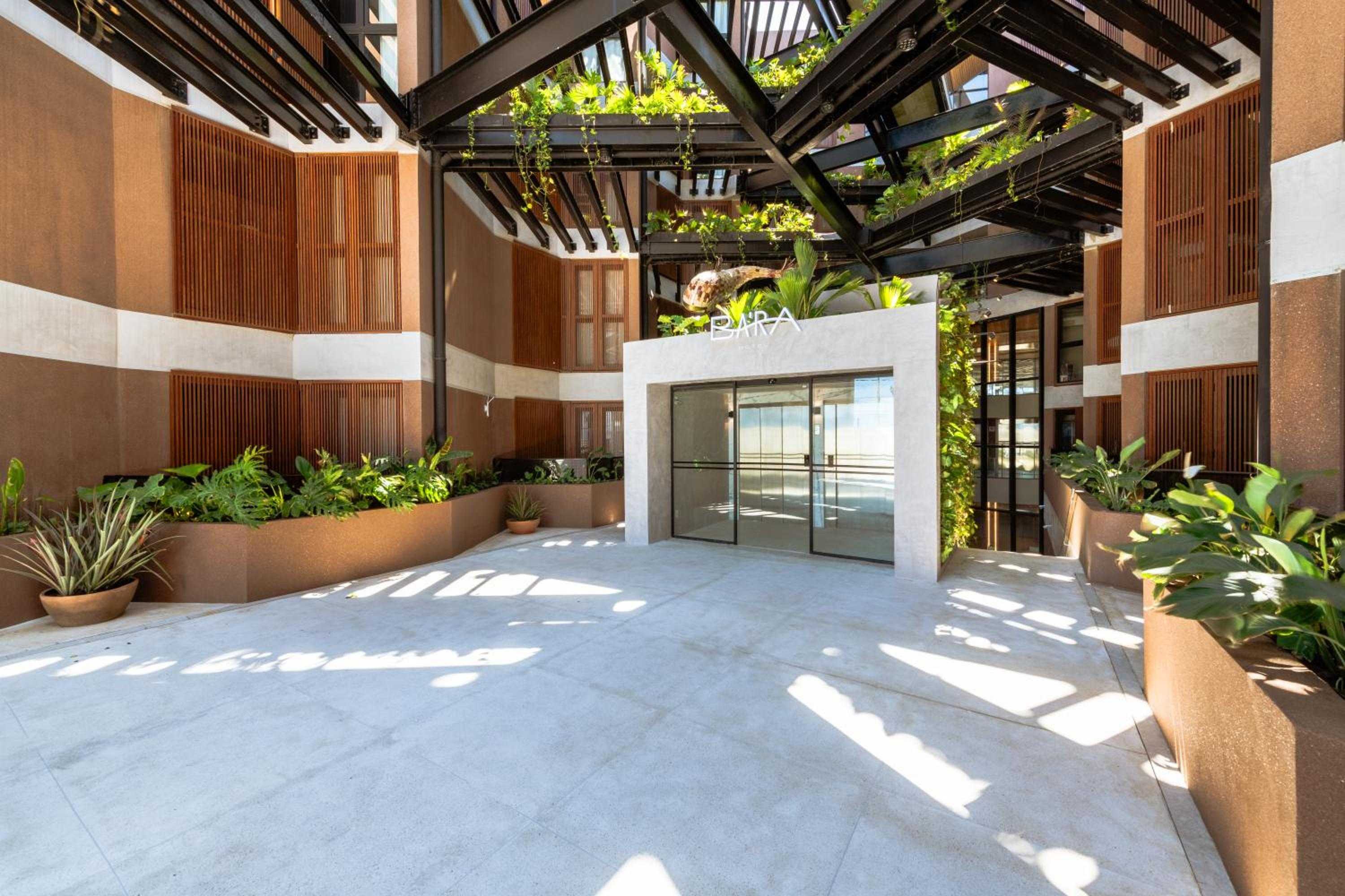 Dappled sunlight filters through the verdant pergola above BA'RA's entrance courtyard, where warm timber screens and lush plantings create an intimate garden sanctuary.