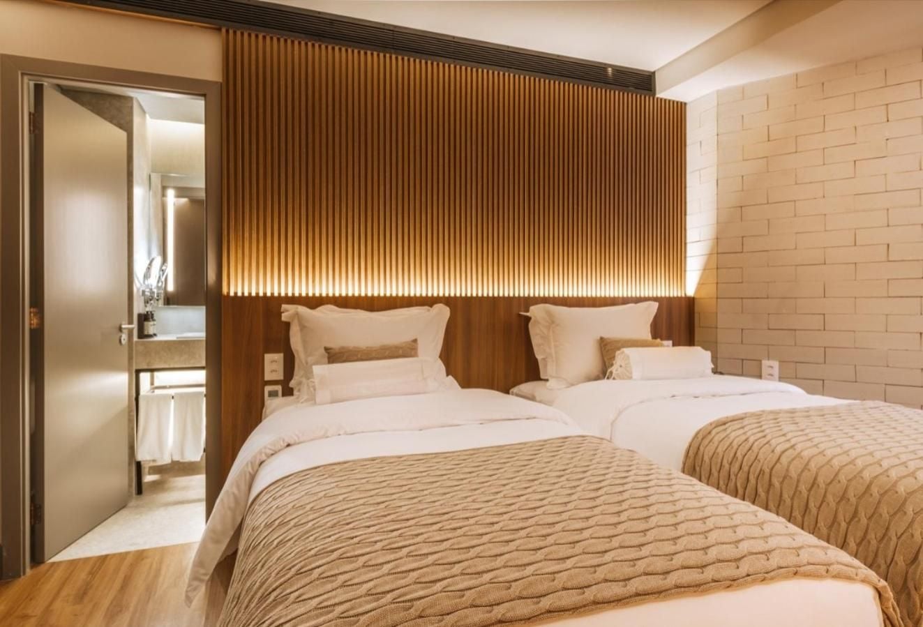 Warm wood slats create intimate ambiance above twin beds, while subway tiles and brass fixtures echo throughout this thoughtfully designed guest room.