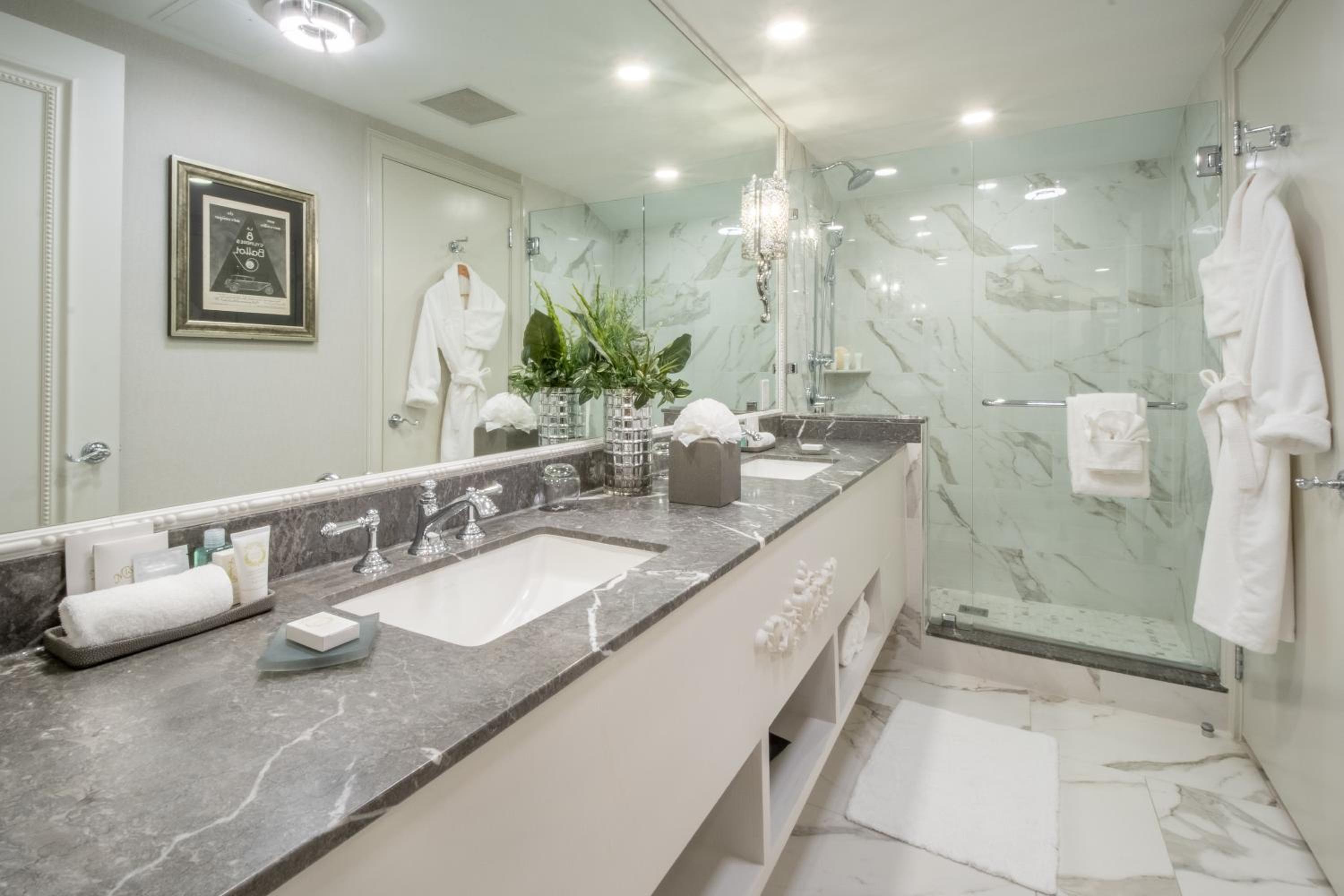 Calacatta marble cascades across walls while crystal chandeliers cast ethereal light over the expansive vanity, where plush robes await like silent butlers.
