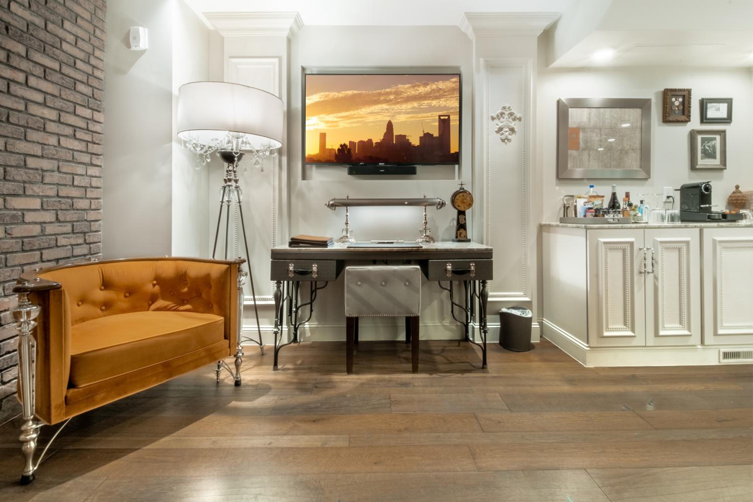 Warm amber leather and exposed brick create an inviting workspace where city skyline views dance across the mounted television at golden hour.