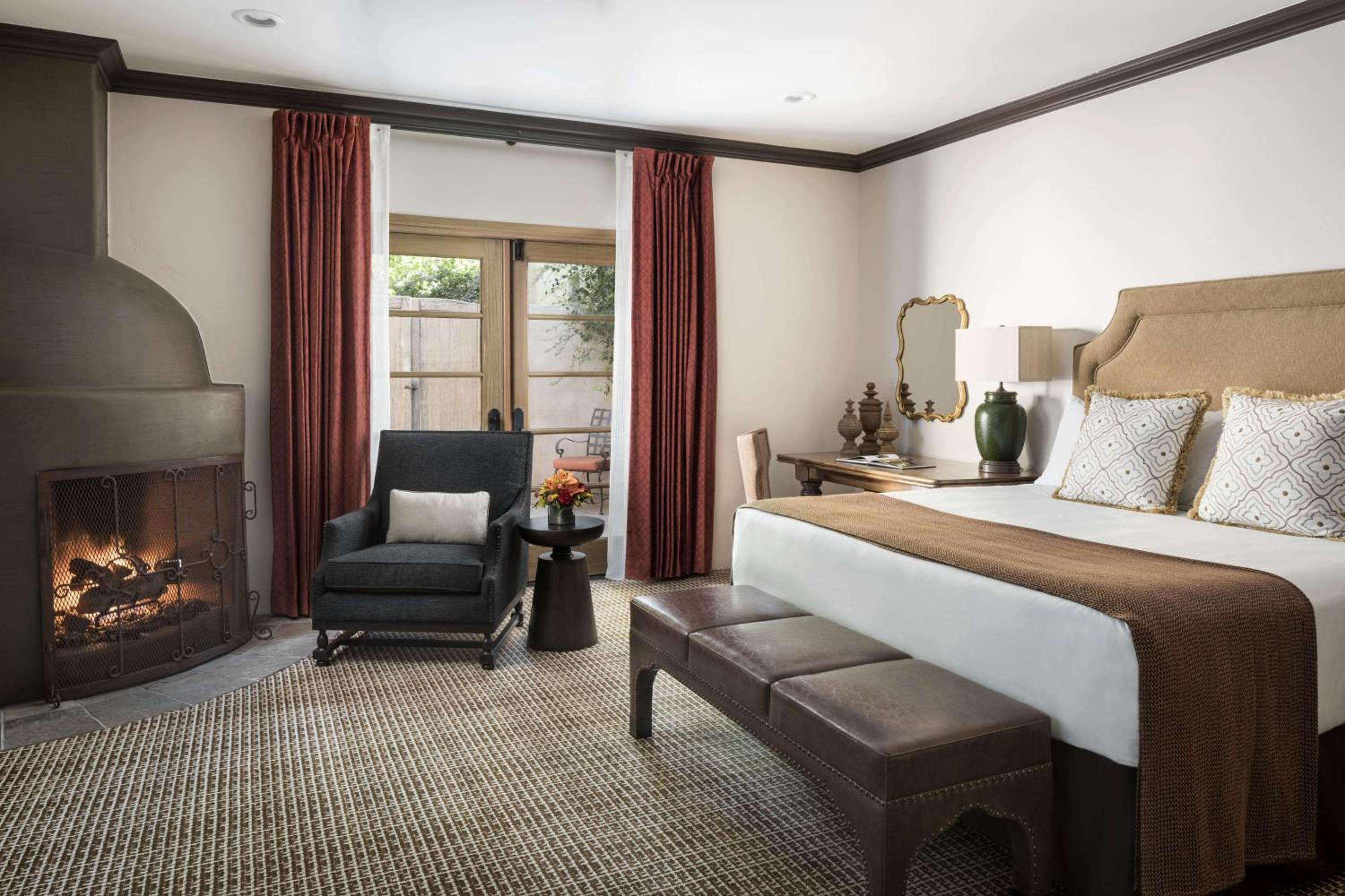 Crackling flames cast warm shadows across this desert sanctuary, where rust-colored curtains frame garden glimpses and woven textures create intimate luxury.