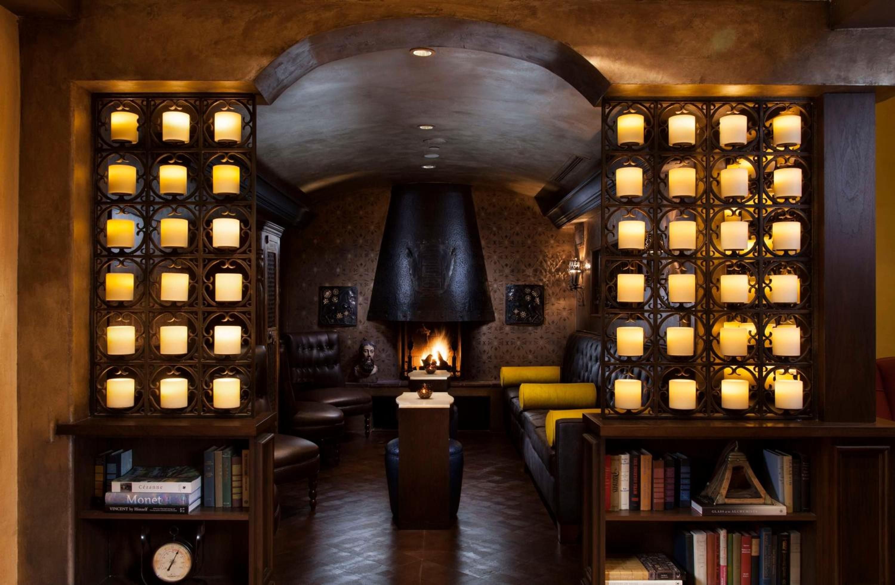 Flickering candles cast golden shadows across wrought-iron grilles in this intimate alcove, where leather seating and crackling fireplace create pure sanctuary.