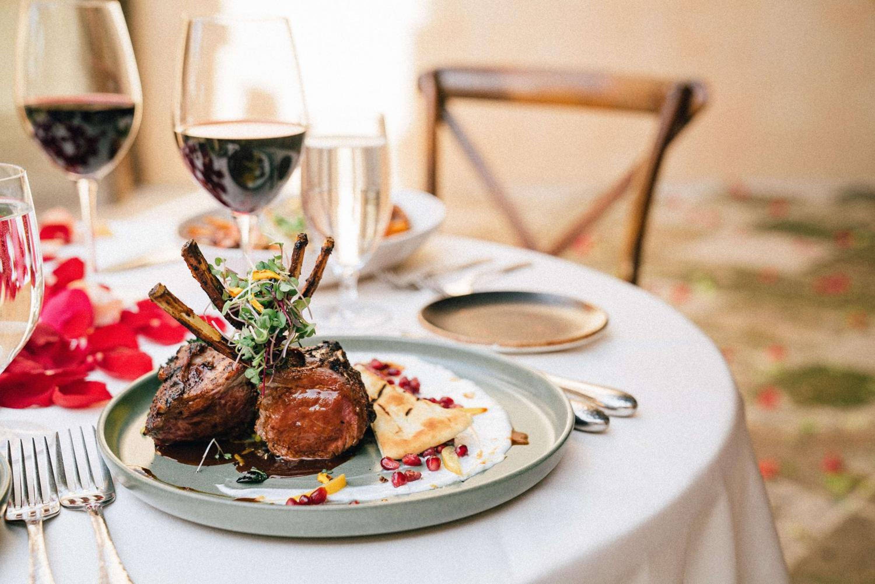Lamb chops crowned with microgreens arrive alongside bold red wine, transforming dinner into an intimate culinary ritual beneath warm desert light.