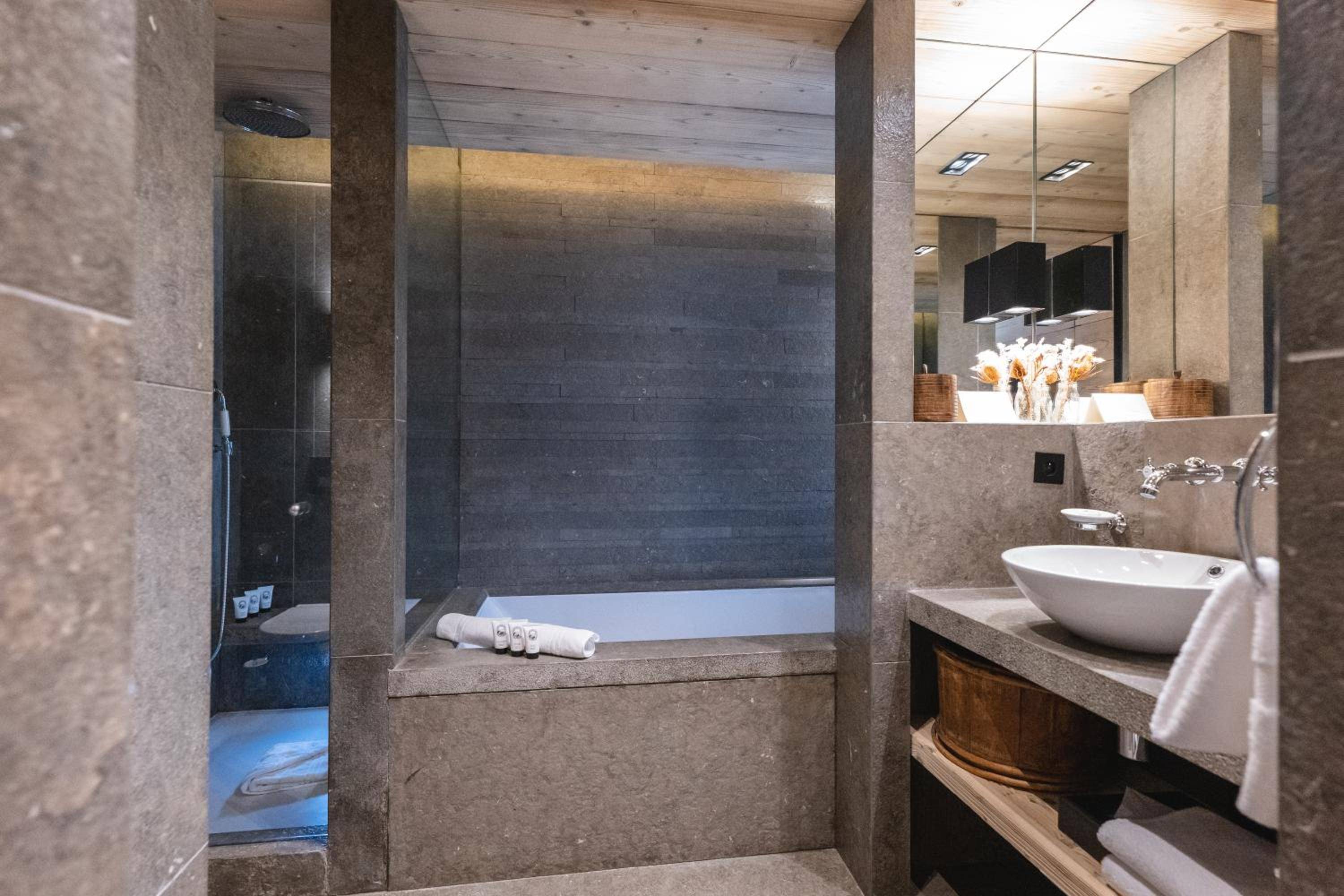 Natural stone and warm wood create a spa-like sanctuary, where the soaking tub becomes a cocoon framed by dramatic lighting and Alpine-inspired materials.