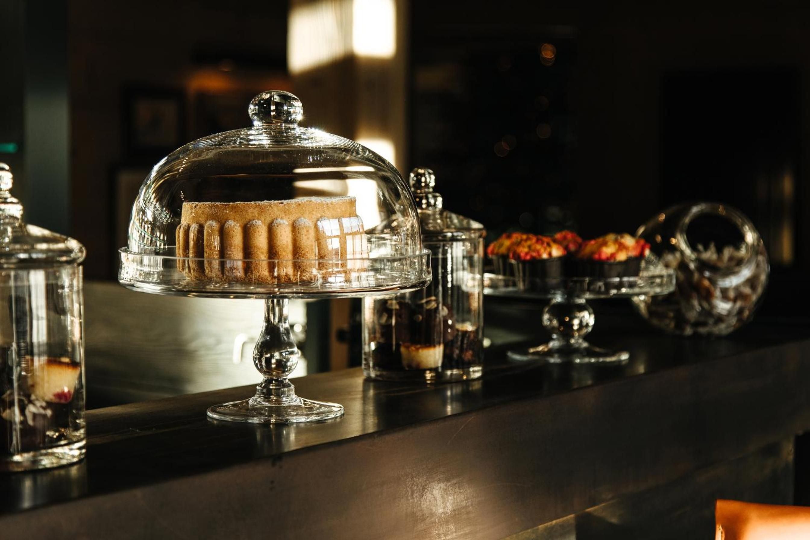 Crystal cake domes showcase delicate pastries along the buffet counter, where golden light catches polished glass and creates an intimate patisserie moment.