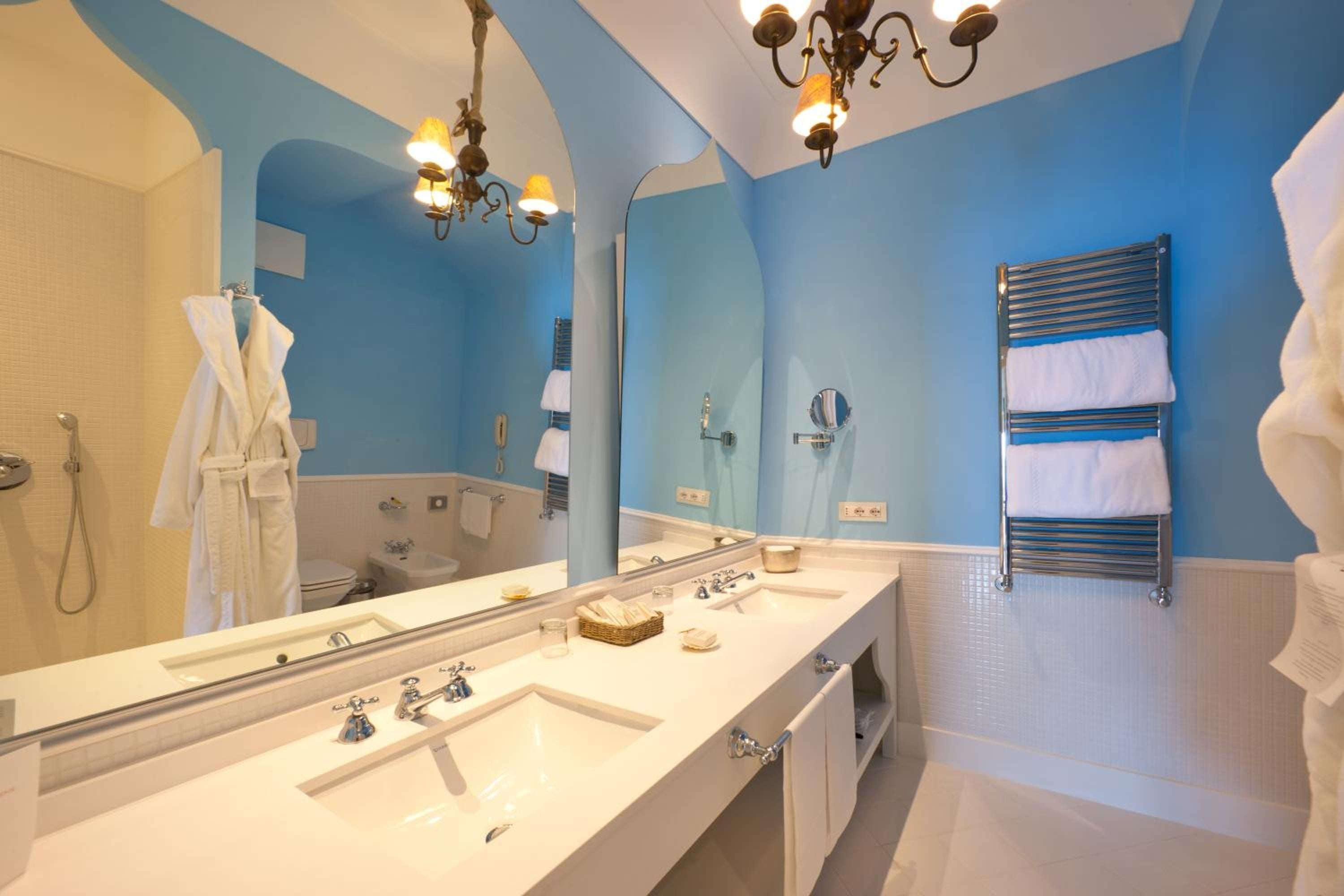 Graceful arches frame azure walls in this Mediterranean-inspired suite bathroom, where marble countertops and vintage brass fixtures create an atmosphere of refined coastal elegance.