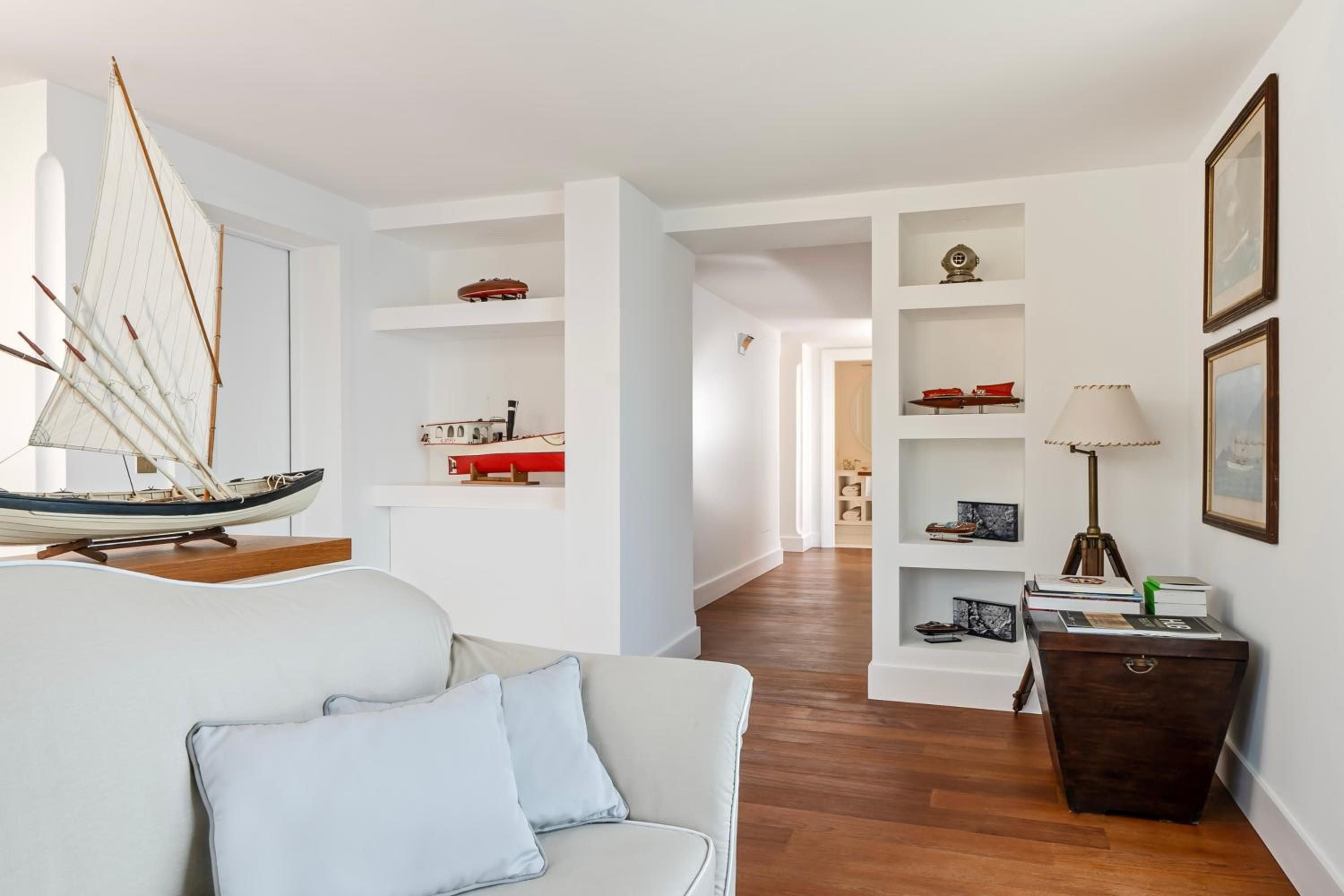 Nautical charm pervades this elegant suite where model sailboats rest on custom shelving, warm wood floors meet crisp white walls, and maritime memories feel authentically curated.