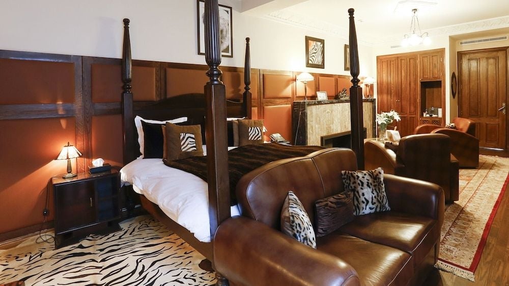 Rich leather seating and a dramatic four-poster bed create an sophisticated safari-inspired retreat, where zebra-print accents and warm wood paneling evoke colonial elegance.