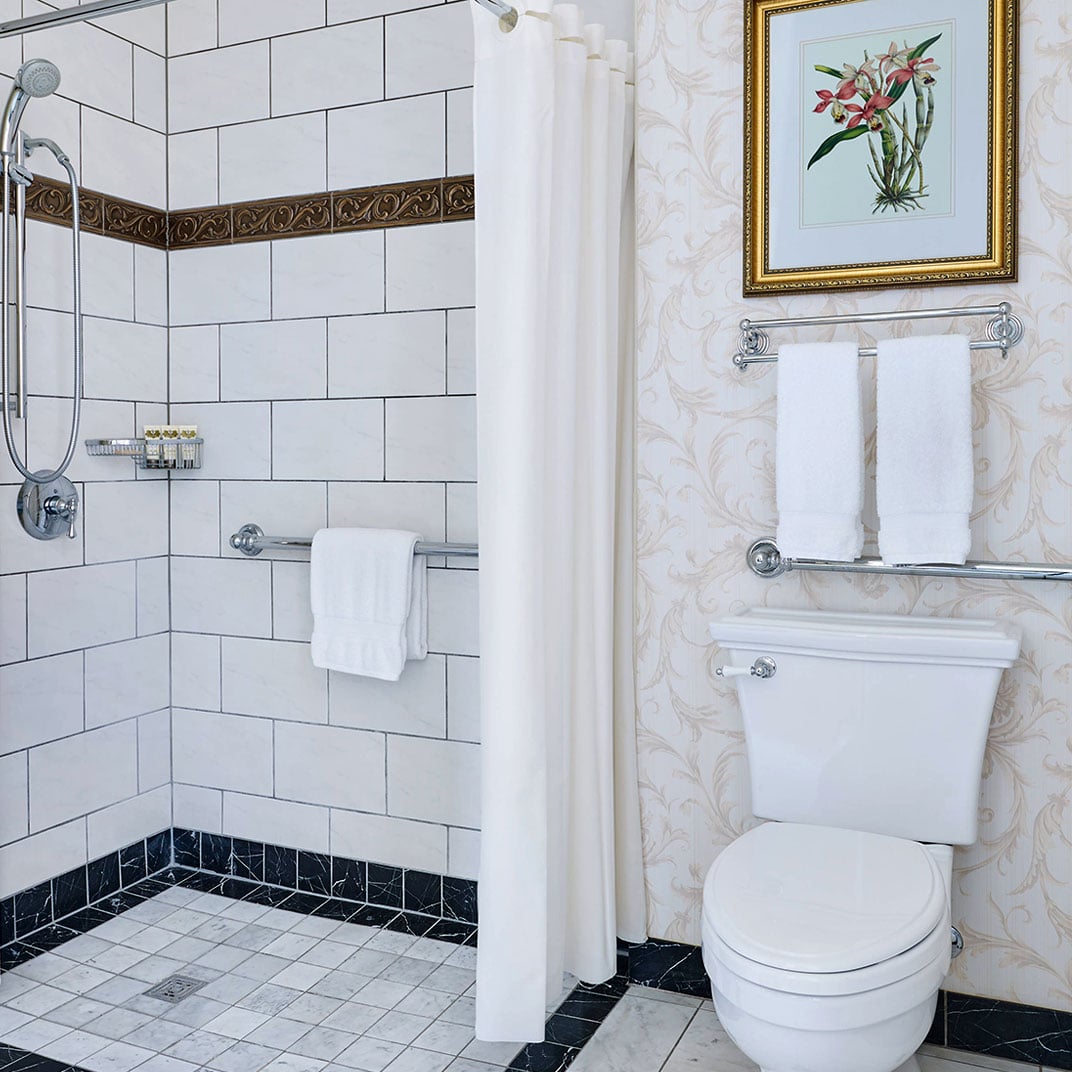 Elegant subway tiles and decorative borders frame the walk-in shower, while botanical artwork and marble-effect wallpaper create a refined, spa-like sanctuary.