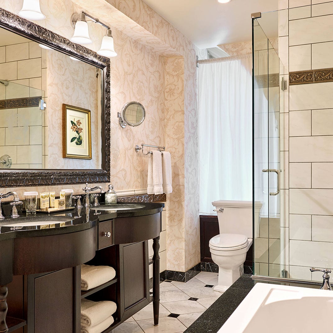 Ornate wallpaper and dark marble vanities create an intimate sanctuary where classical elegance meets modern luxury in this beautifully appointed guest bathroom.