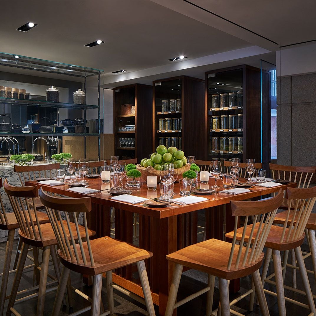 Warm wood tones and flickering candlelight create an intimate culinary library, where seasonal centerpieces of green apples complement the restaurant's sophisticated farm-to-table philosophy.