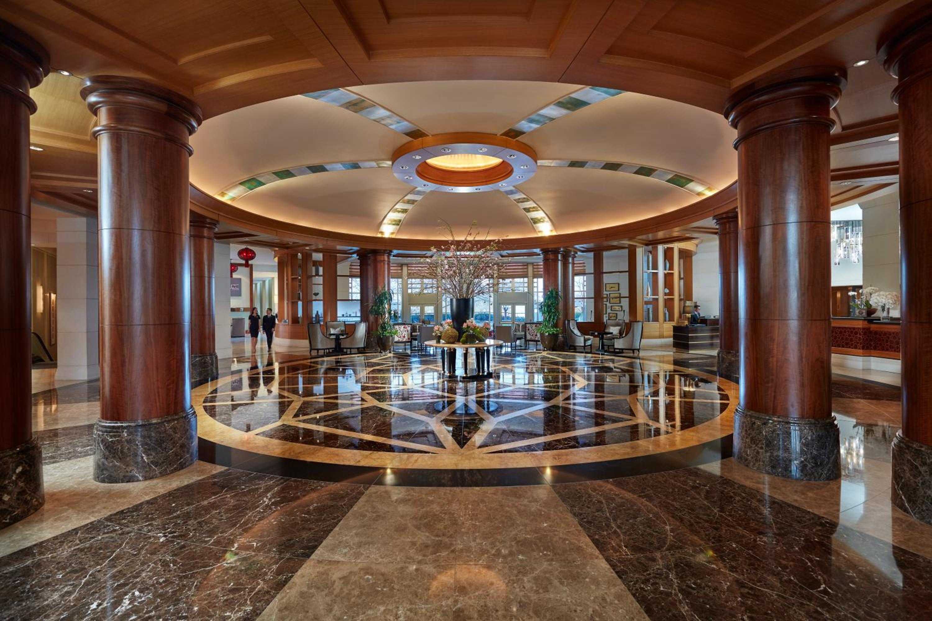 Gleaming marble floors radiate outward beneath soaring columns and a dramatic coffered ceiling, where warm lighting creates an intimate grandeur in the rotunda-style entrance.