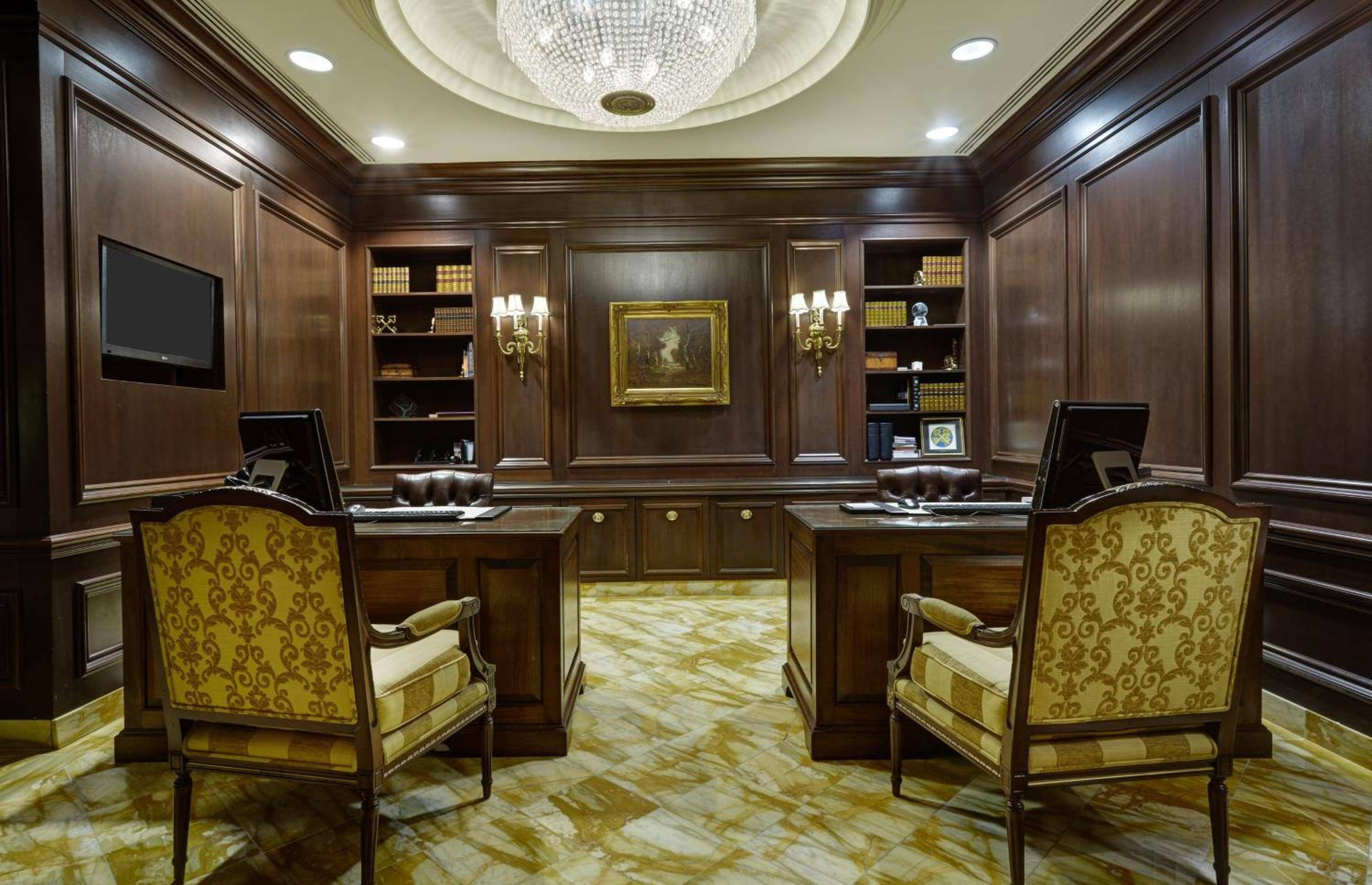 Rich mahogany paneling and gilded sconces create an atmosphere of gravitas in this executive office space, where crystal chandeliers cast warm light over marble floors.