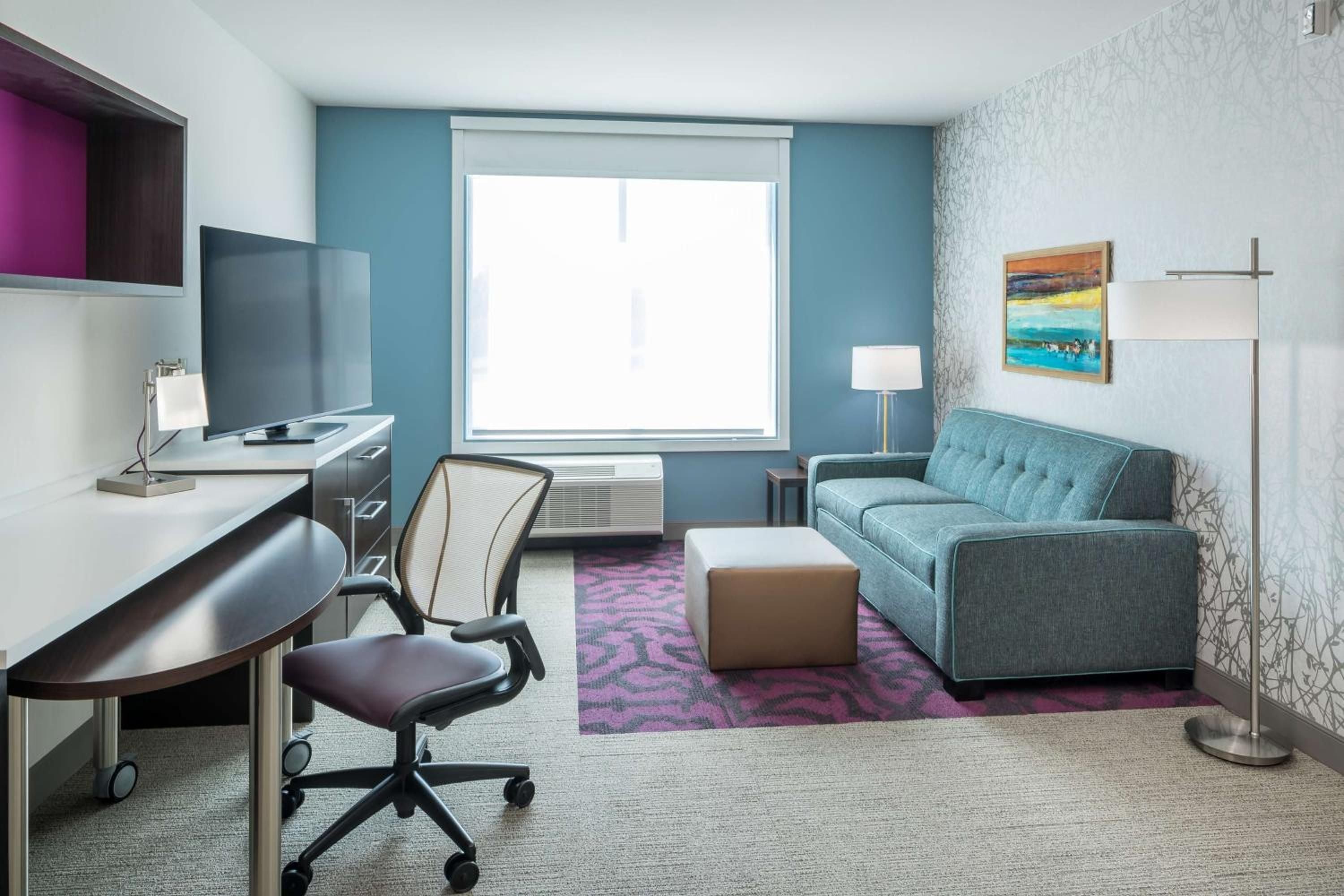 Teal accents and geometric patterns create a sophisticated living space where natural light floods through oversized windows, complementing the thoughtful blend of work and relaxation zones.