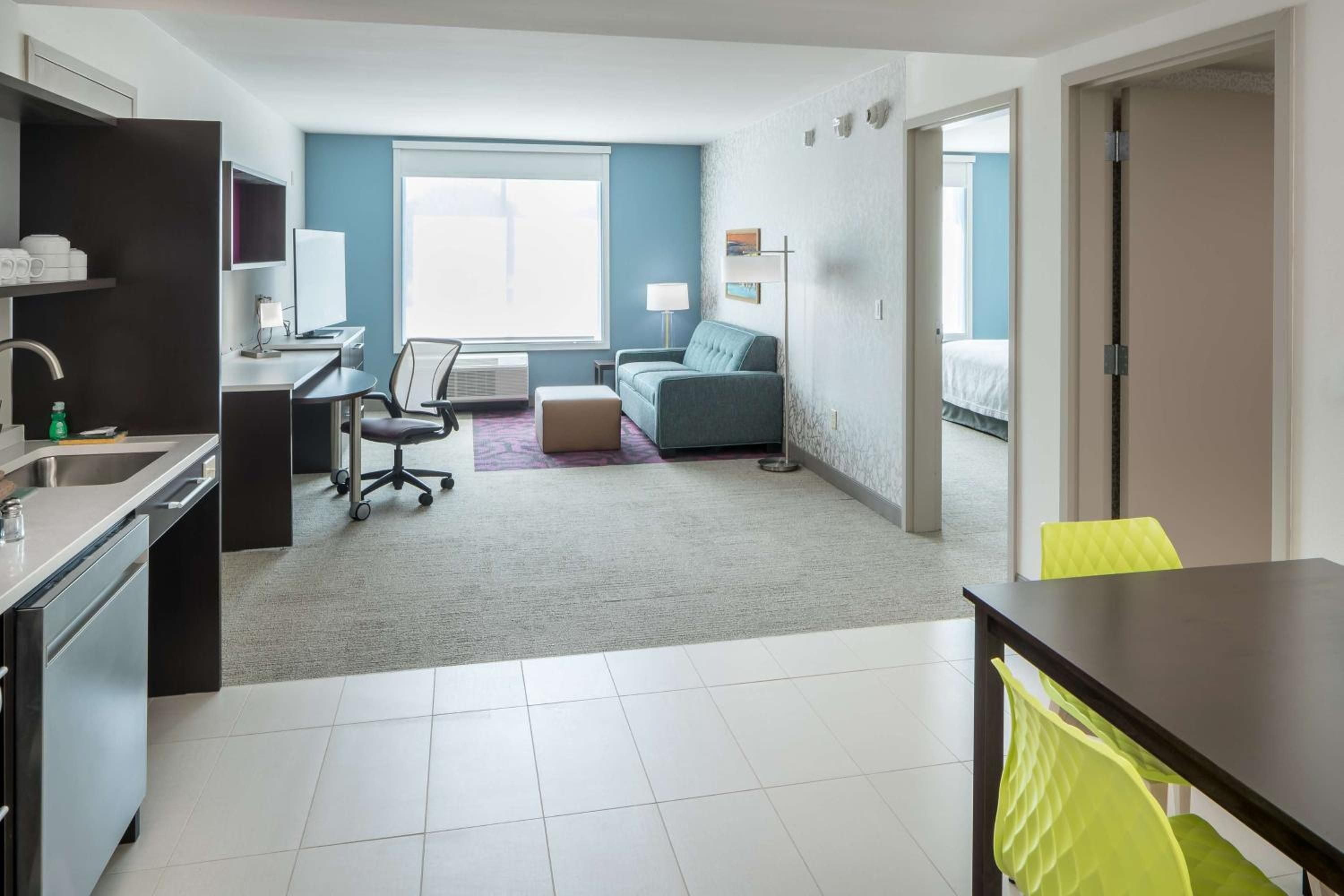 Bright yellow chairs punctuate the sophisticated living space, where teal accents and clean lines create a fresh, contemporary atmosphere perfect for extended stays.